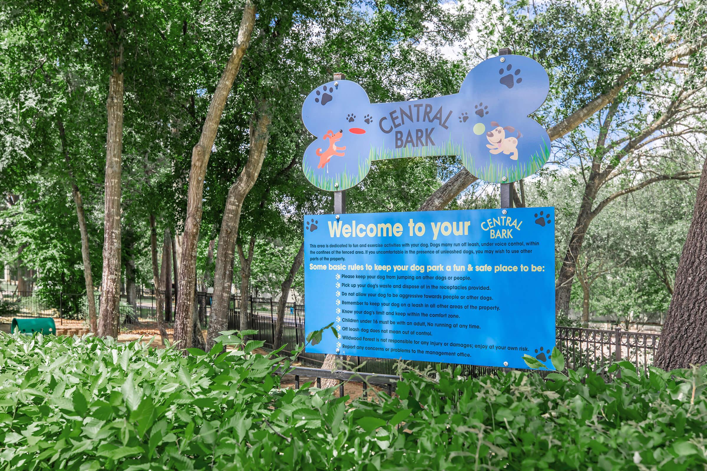 Sign at Central Bark dog park welcoming visitors and outlining basic rules for a safe and enjoyable experience. The sign features playful dog-themed graphics and is surrounded by greenery, creating a friendly atmosphere for pets and their owners.