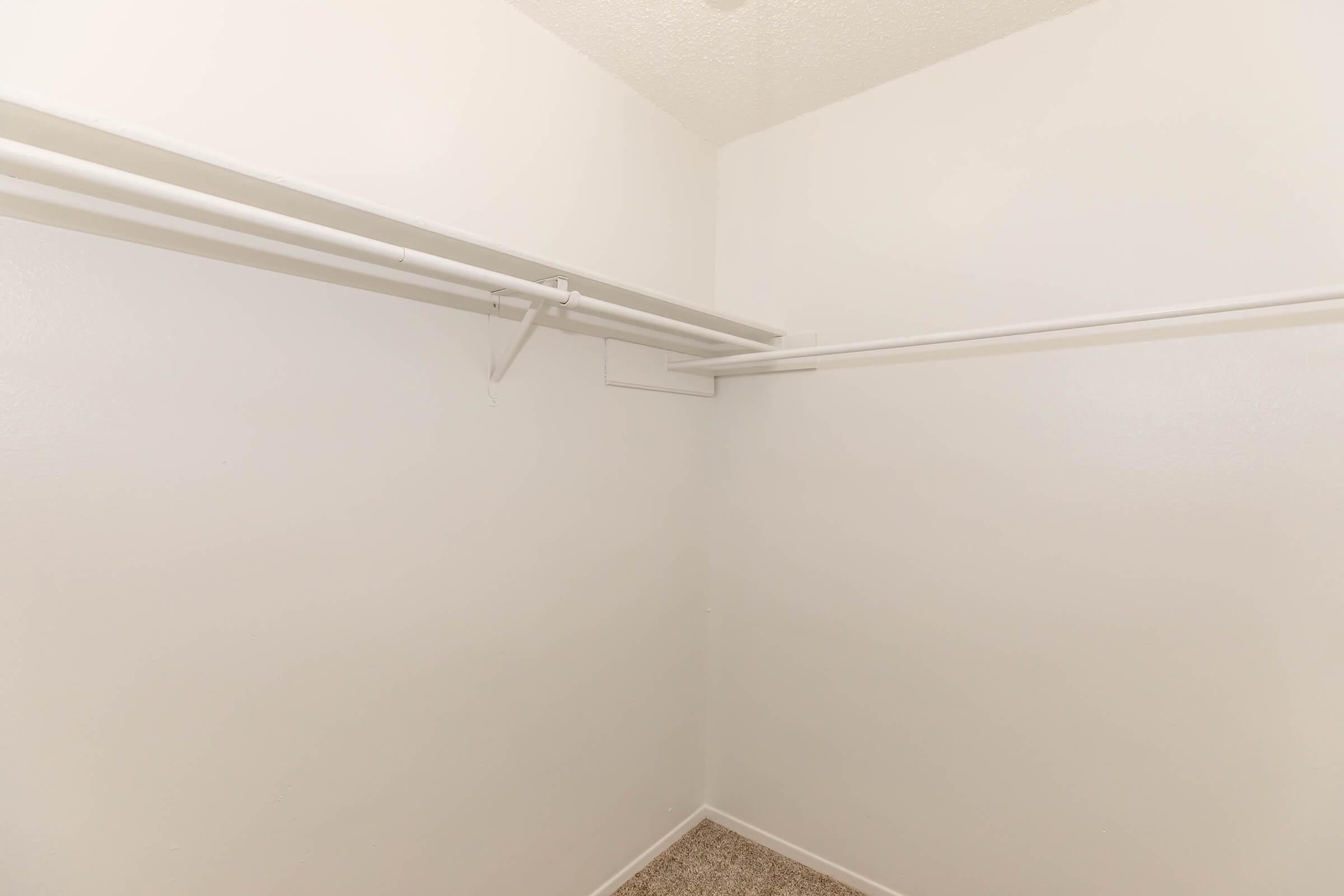 Empty closet with white walls, a beige carpet, and a single shelf with hanging rods. The space appears clean and organized, suitable for storage.