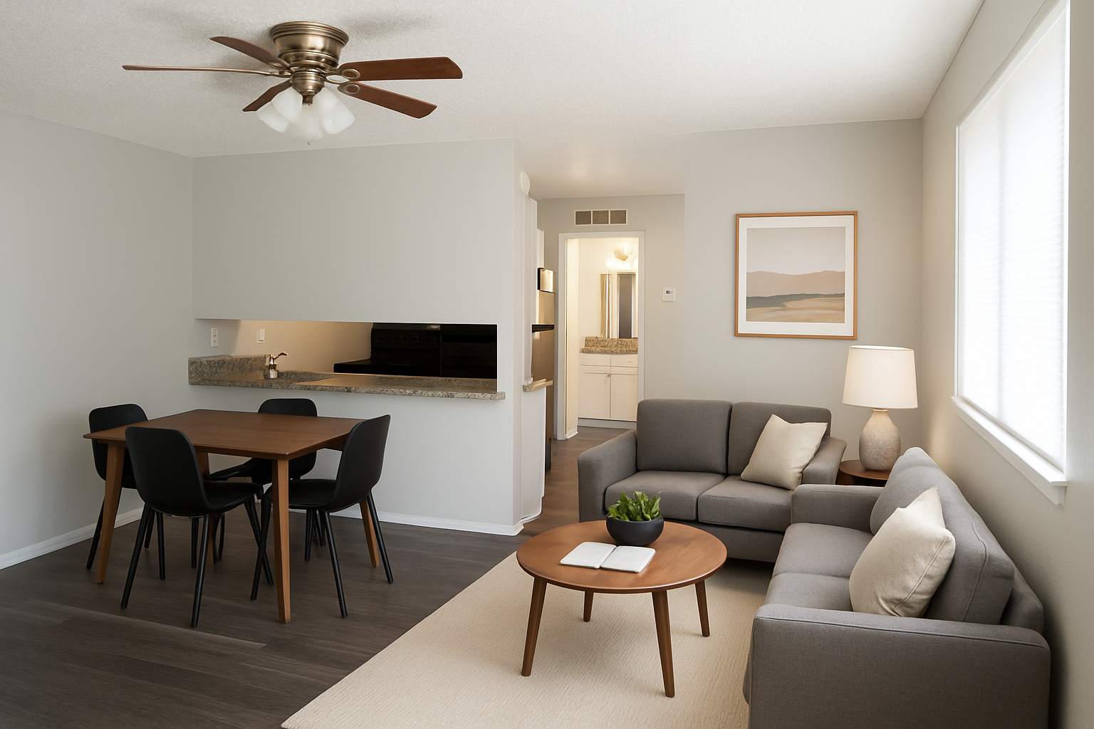 A modern living room with a light gray color scheme featuring a sofa, coffee table, and armchair. In the background, there's a dining area with a wooden table and black chairs. A ceiling fan hangs above, and there's a light gray wall with a framed art piece. A doorway leads to a hallway with additional rooms.