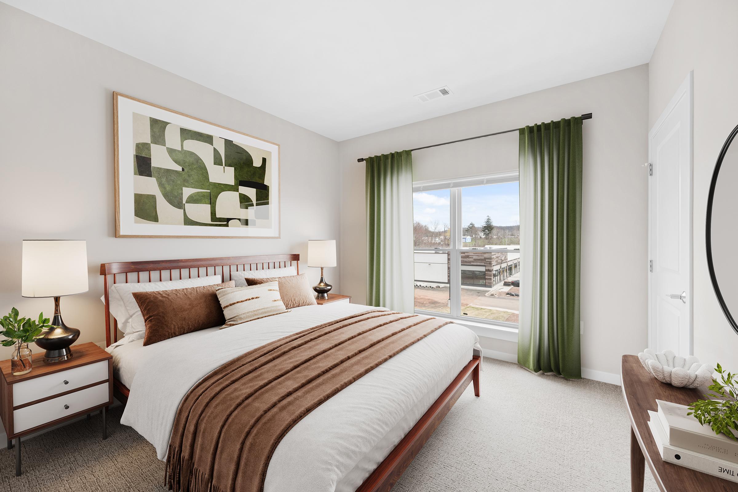 A well-decorated bedroom featuring a wooden bed frame with a white and brown bedding set. There are two bedside tables with lamps, green curtains framing a window that offers a view outside, and a large wall art piece above the bed. The overall color scheme is neutral with earthy tones.