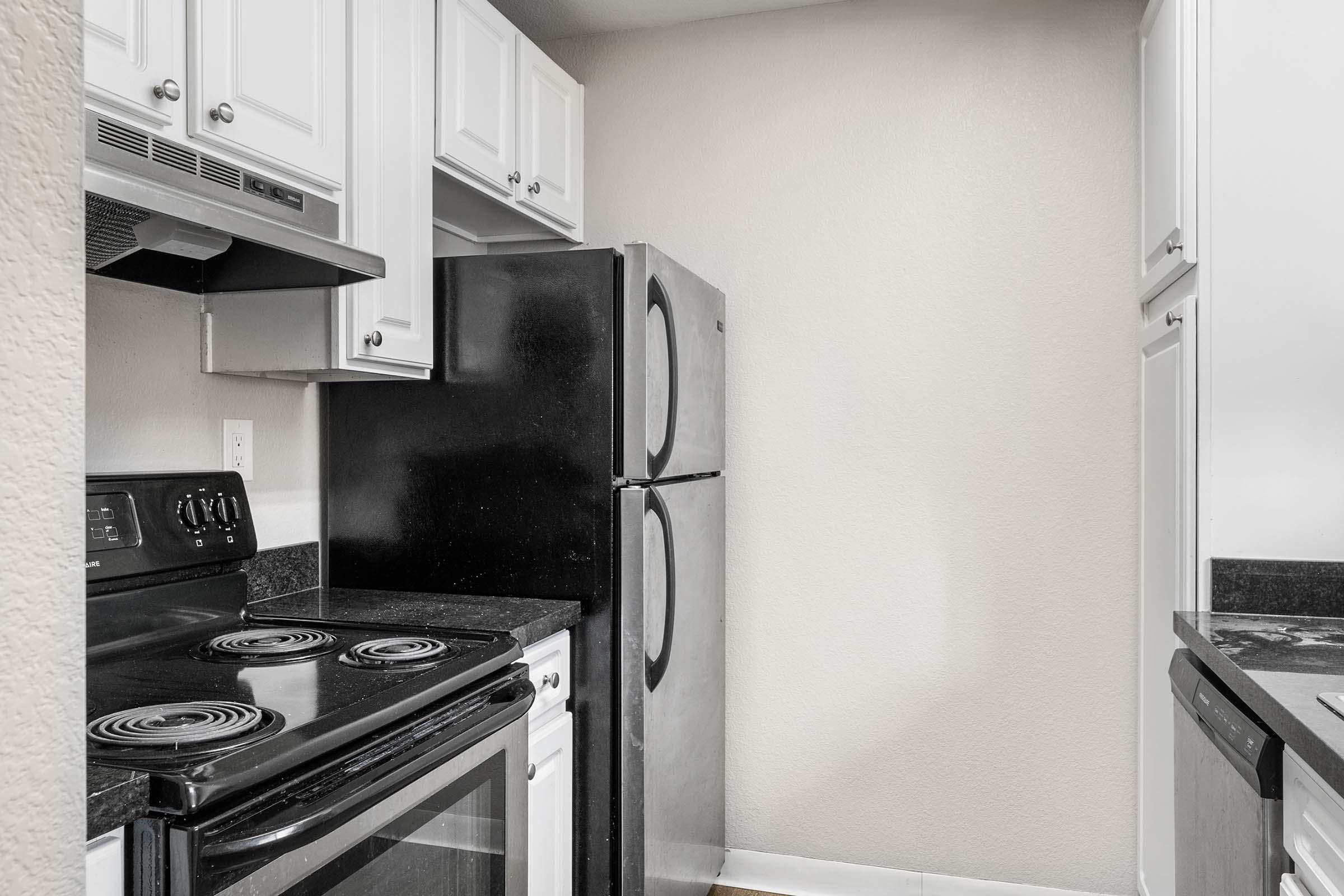 A modern kitchen featuring black appliances, including a stove and refrigerator. The cabinetry is white, and the countertops are black. The space is well-organized with a clean, minimalist design, emphasizing functionality. Light-colored walls enhance the brightness of the area.