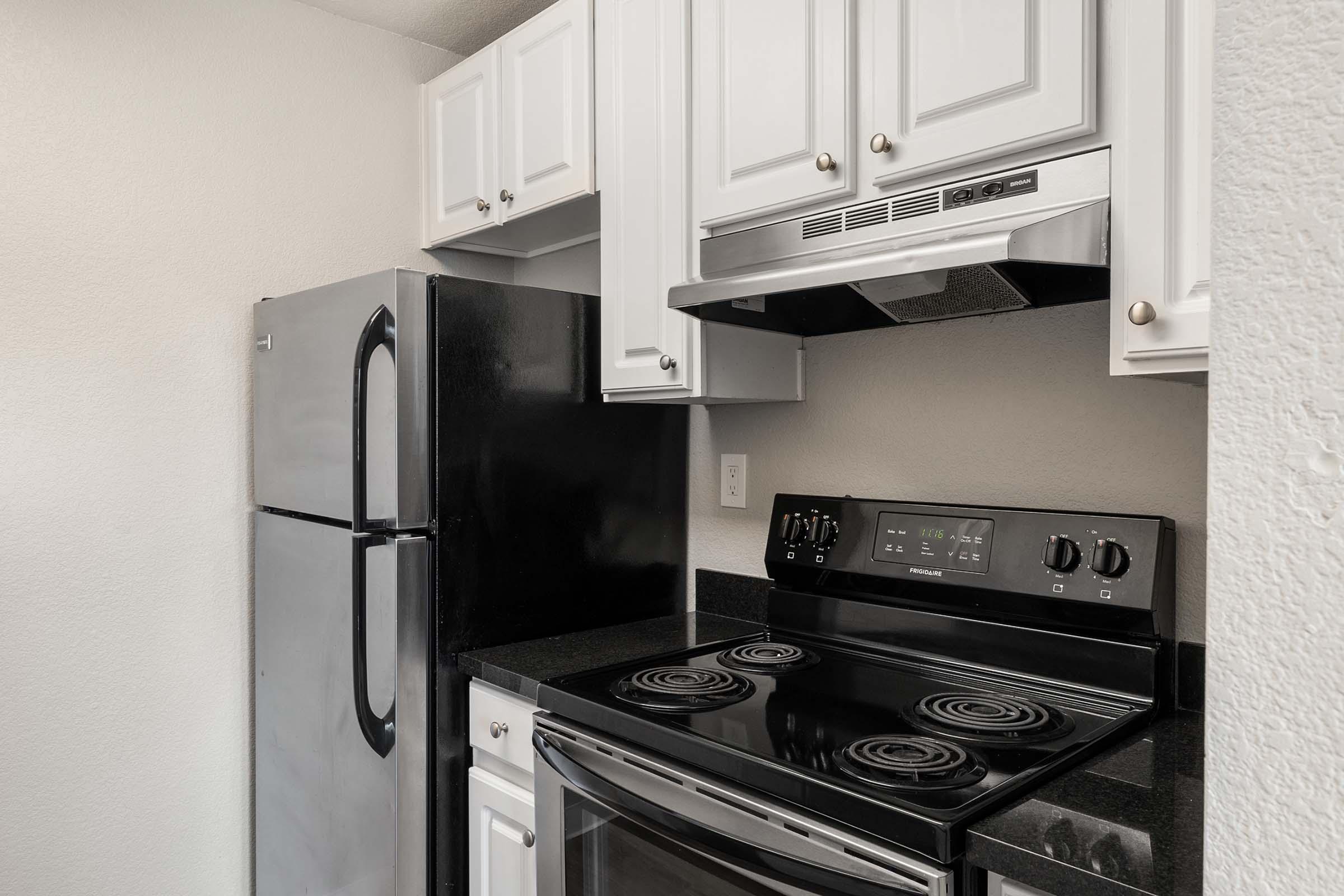 A modern kitchen featuring black appliances including a refrigerator and an electric stovetop with an oven. White cabinets and a black countertop complete the design, providing a sleek and functional cooking space. The walls are painted light, enhancing the overall brightness of the area.
