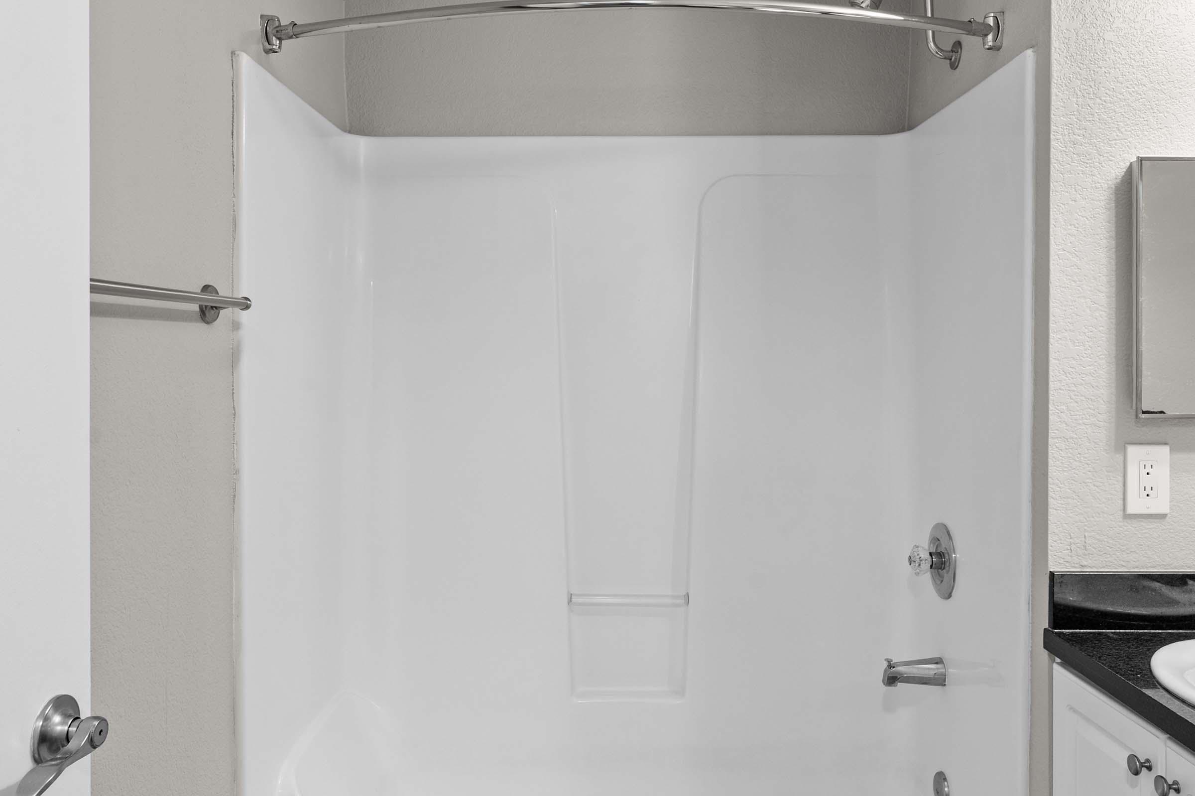 A clean, modern shower stall with a white fiberglass interior, a chrome showerhead, and a sleek faucet. The shower is enclosed by a curved shower rod, and the walls are smooth and unadorned, creating a minimalistic look. The surroundings appear well-maintained with neutral color tones.