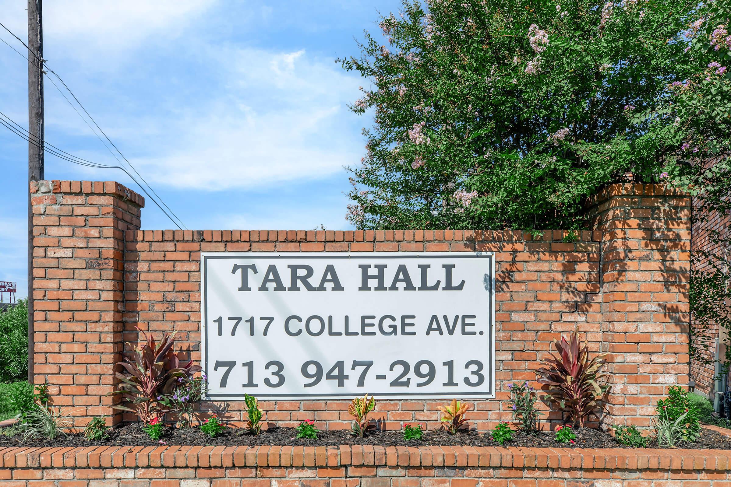 Sign for Tara Hall located at 1717 College Ave, featuring a brick structure with decorative plants. The sign includes the phone number 713-947-2913 and is set against a blue sky with scattered clouds.