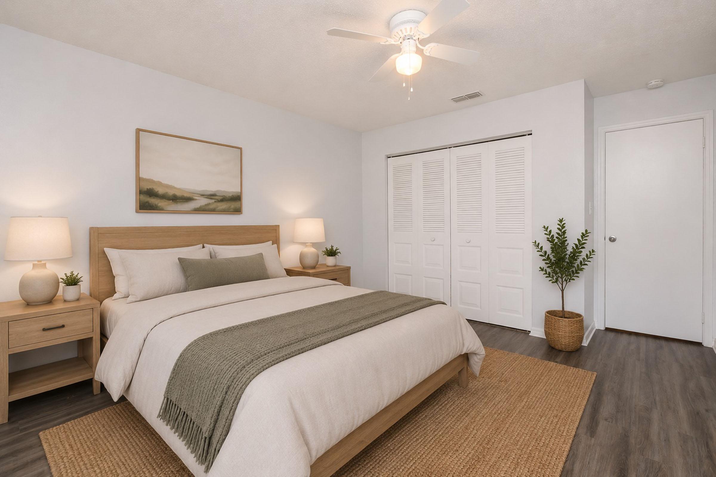 A cozy bedroom featuring a wooden bed frame with neutral bedding, two bedside tables with lamps, and a modern painting above the bed. There are white closet doors and a potted plant in a woven basket, with a jute rug on a dark wooden floor, creating a welcoming and serene atmosphere.
