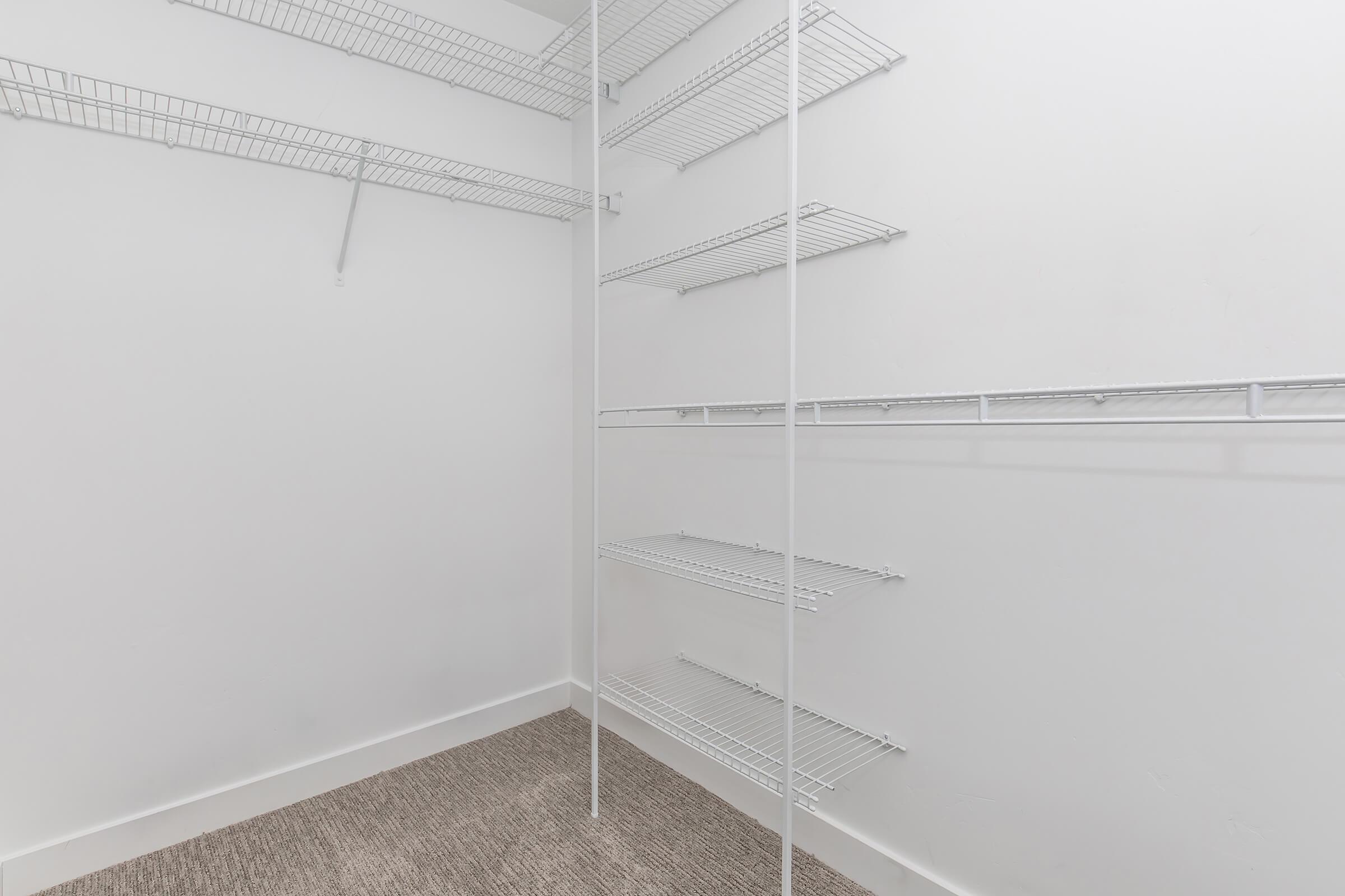 Empty closet with white wire shelving and a beige carpeted floor. The walls are white, and the shelving is organized in a spacious layout, providing ample storage options.
