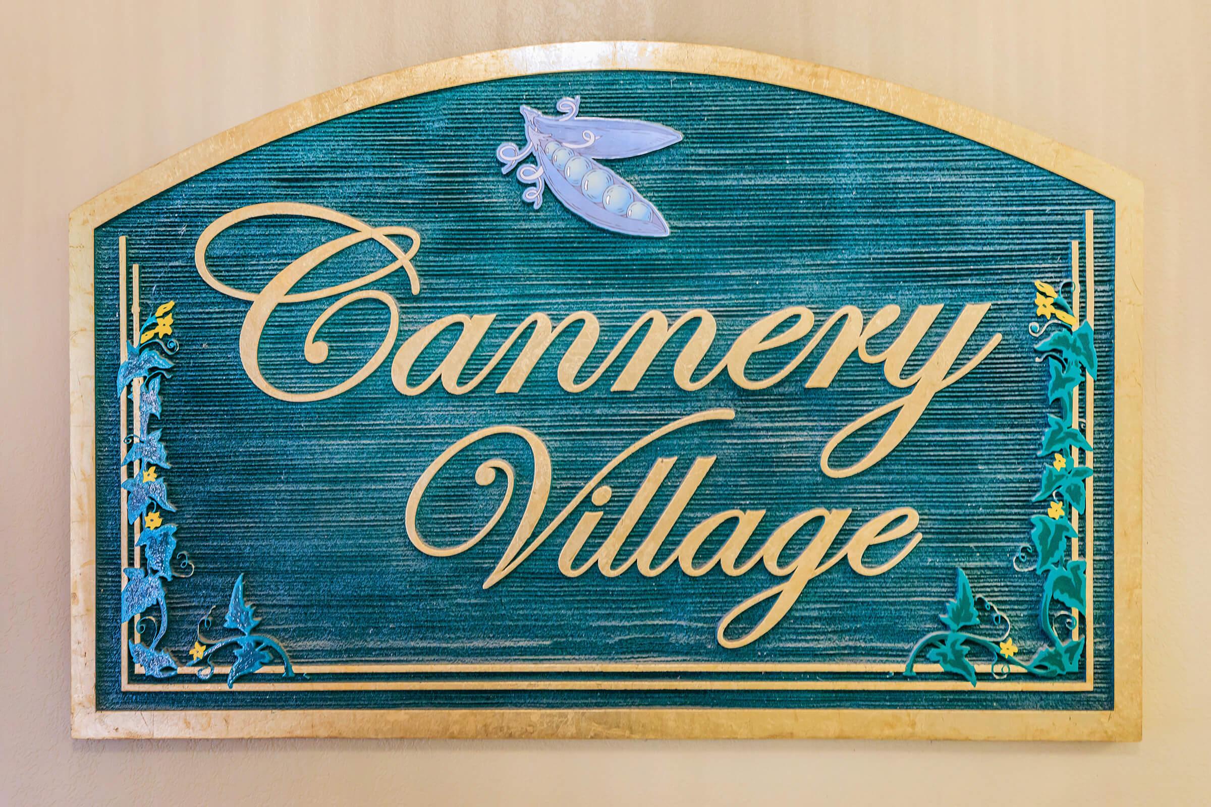 A decorative sign reading "Cannery Village" with blue and green colors, featuring a graphic of a pea pod at the top and ornamental scrollwork along the edges.