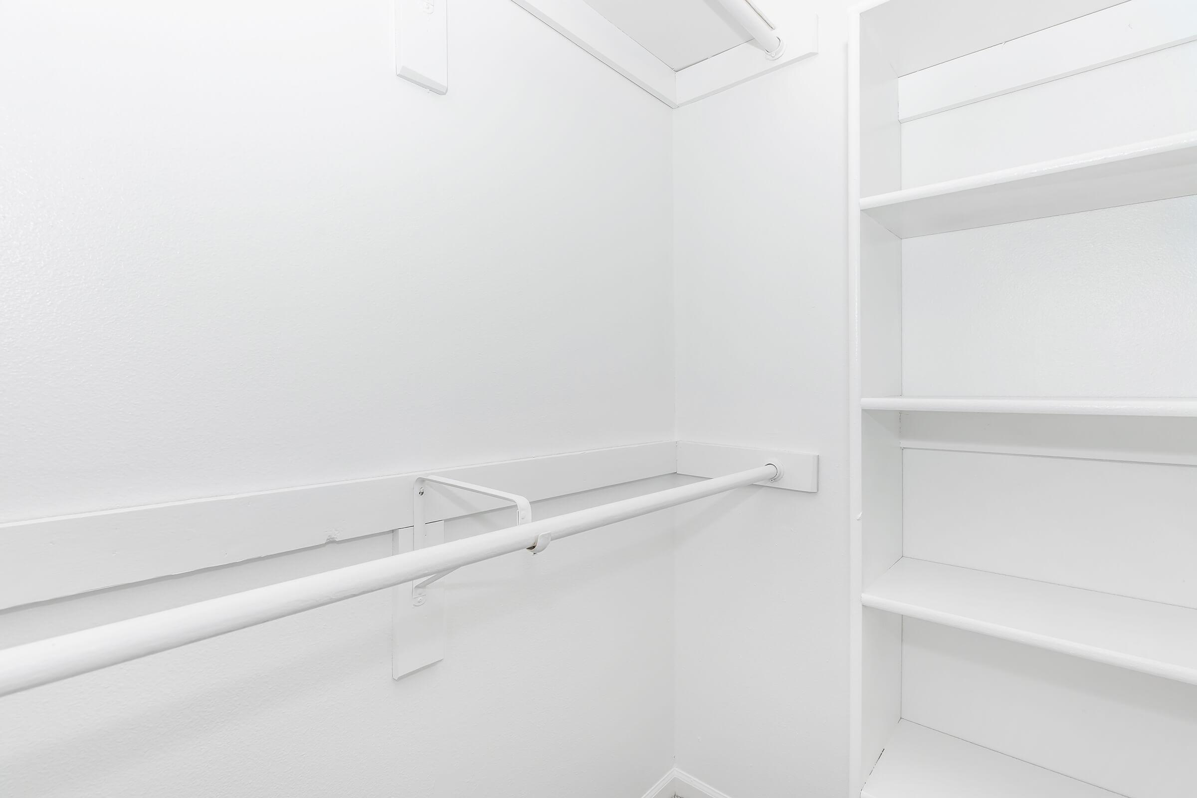 Empty white closet interior featuring a single hanging rod and several shelves, all in a clean white finish, creating a minimalist and spacious look.