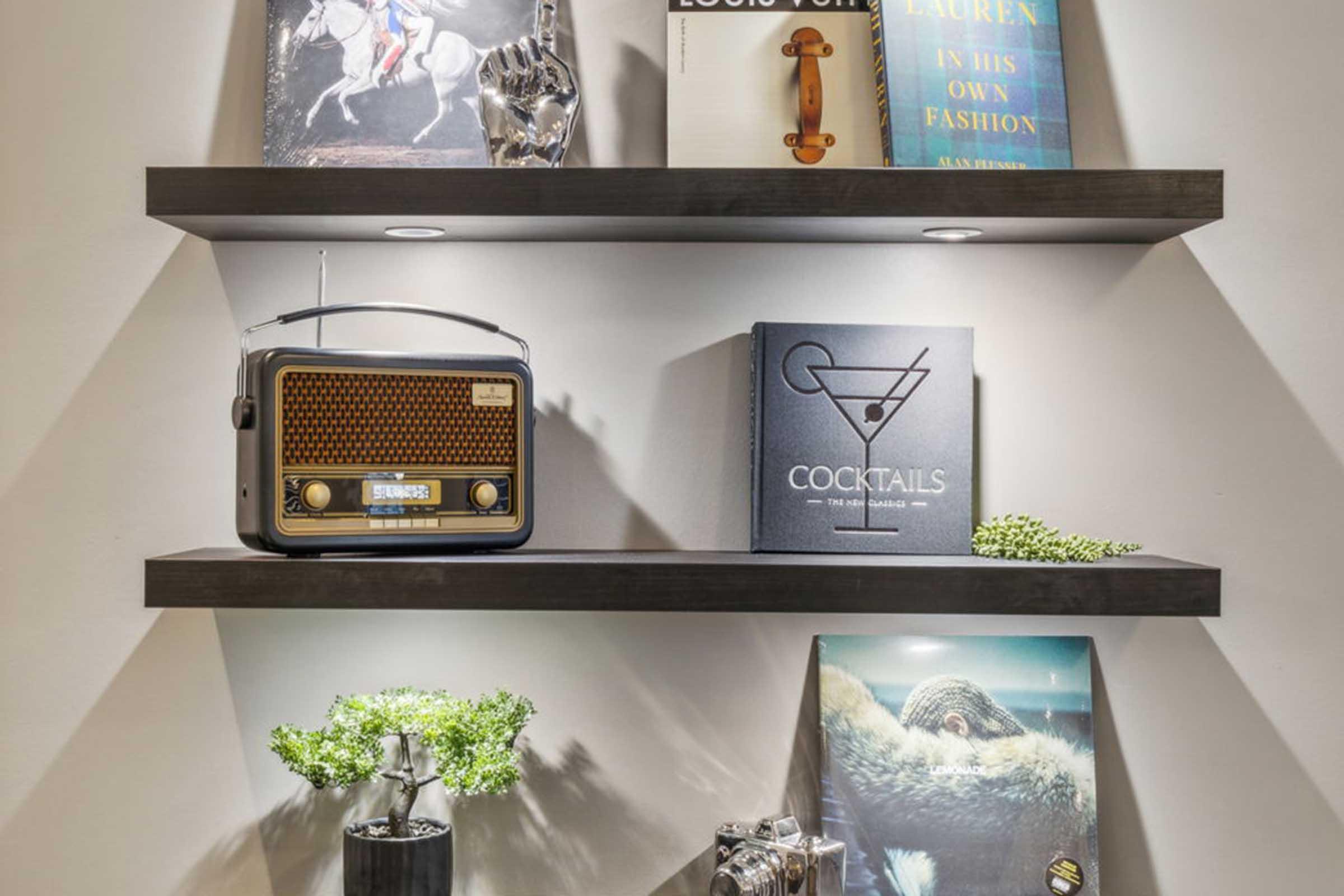 A stylish shelf displaying a vintage radio, books on fashion and cocktails, and decorative items. The shelf is illuminated with soft lighting, enhancing the modern aesthetic of the setup.