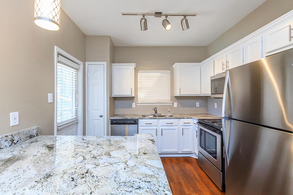 Modern kitchen featuring white cabinetry, stainless steel appliances, and a granite countertop. A sleek light fixture hangs from the ceiling, and natural light filters through a window. The design is contemporary and well-organized, with a focus on functionality and style.