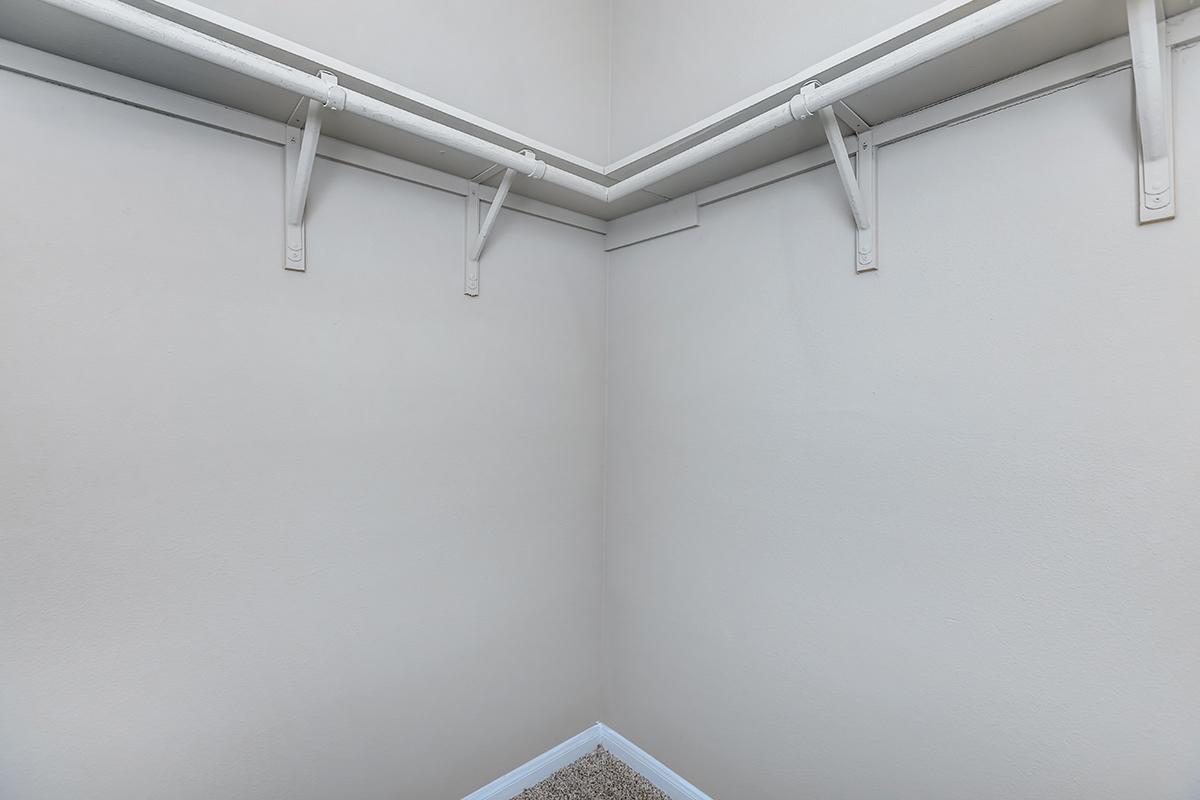 Empty closet corner with light-colored walls and white shelves supported by brackets, offering a spacious and uncluttered look. The floor is carpeted, creating a cozy atmosphere in a simple and minimalist design.