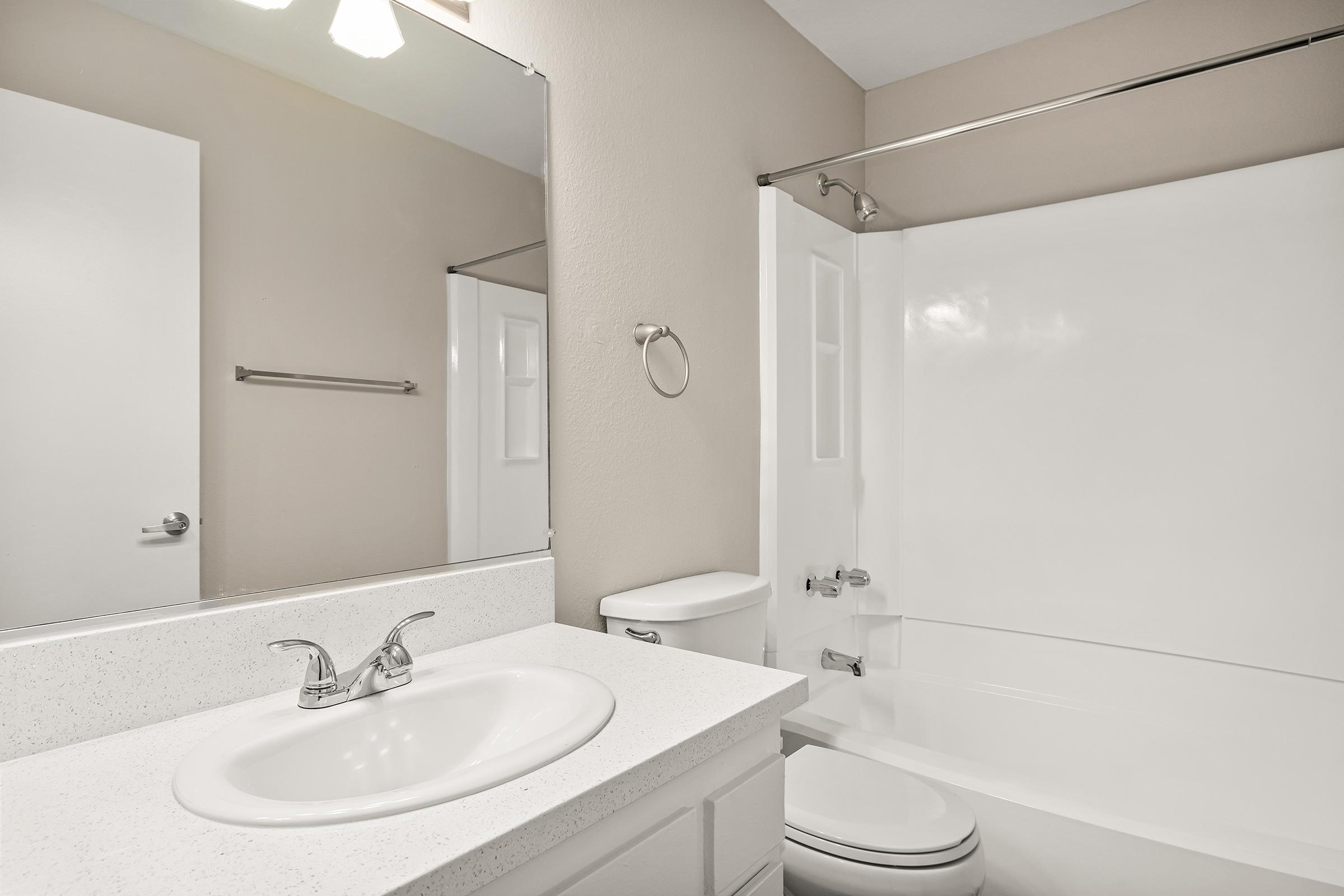 A clean and modern bathroom featuring a white sink with a sleek faucet, a large mirror, a bathtub with a shower curtain, and a toilet. The walls are painted a neutral color, and there is a towel rack beside the sink. Soft lighting enhances the fresh and inviting atmosphere of the space.