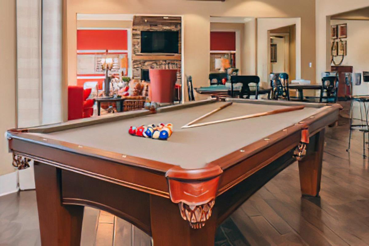 A well-lit game room featuring a pool table with colorful balls arranged on top. In the background, there's a seating area with a fireplace, plush couches, and chairs, creating a cozy atmosphere. The room has hardwood floors and large windows, enhancing the spacious feel.