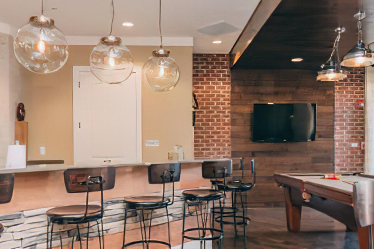 A modern interior featuring a stylish bar area with circular pendant lights, high stools, and a wooden wall. A television is mounted on the wall, and there is a pool table in the foreground. The design combines elements of brick and light wood, creating a warm and inviting atmosphere.