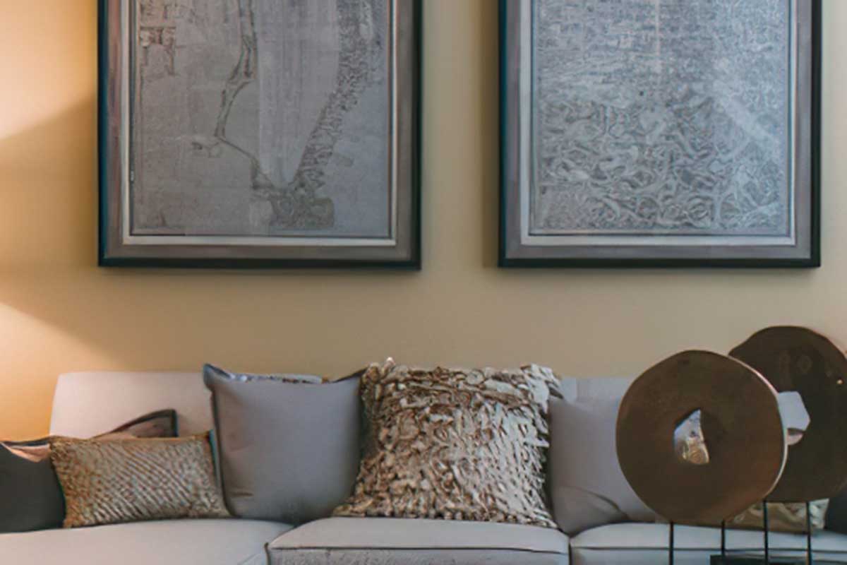 A cozy living room scene featuring a light-colored sofa adorned with decorative pillows. Two large framed artworks hang on a warm-toned wall, and a decorative sculpture sits beside the sofa, adding an artistic touch to the space. Soft lighting creates an inviting ambiance.