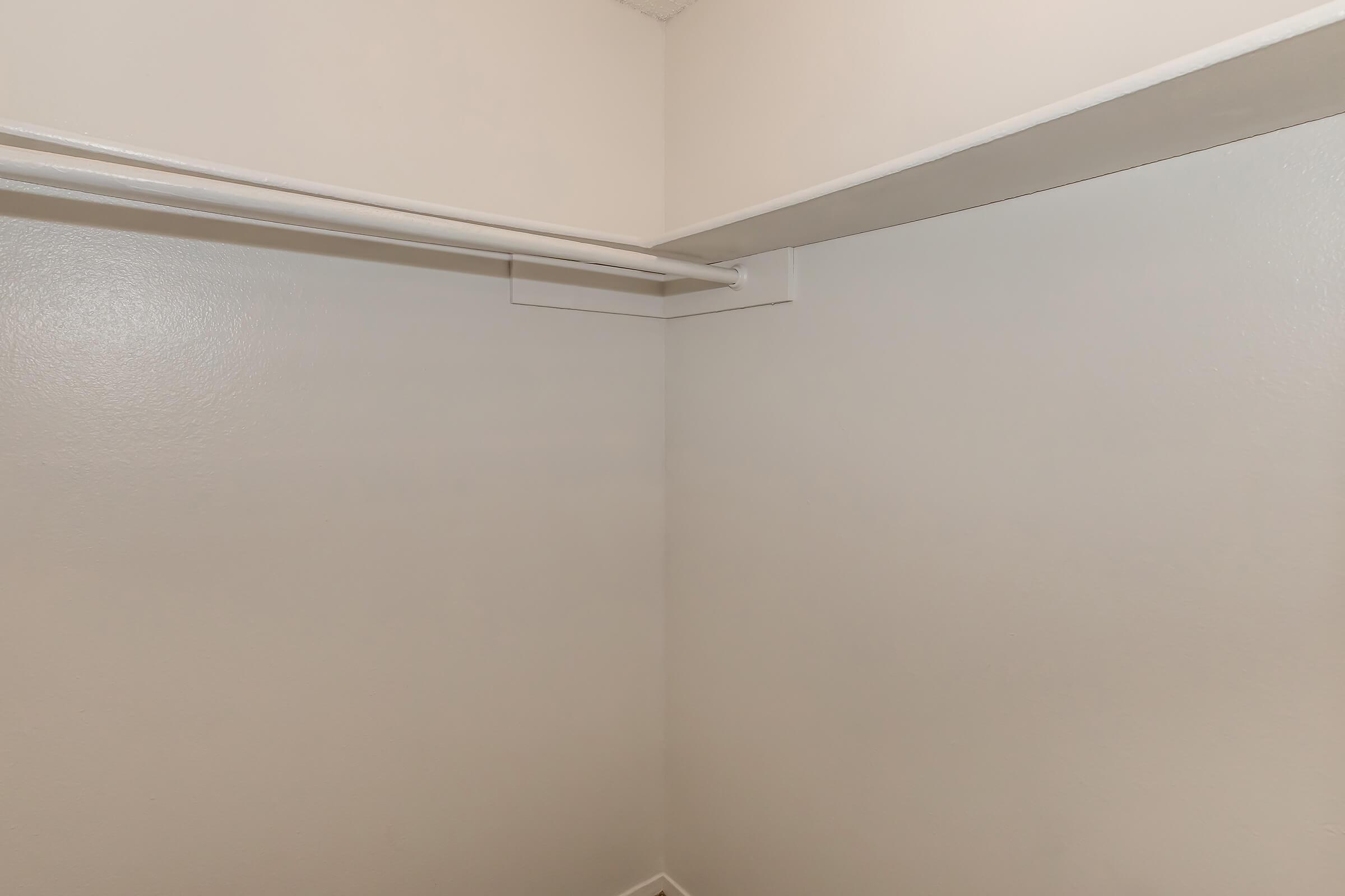 A corner of a closet featuring light-colored walls, a shelf above, and a clothing rod along the top. The space appears empty and well-lit, highlighting the clean, neutral aesthetic of the interior.