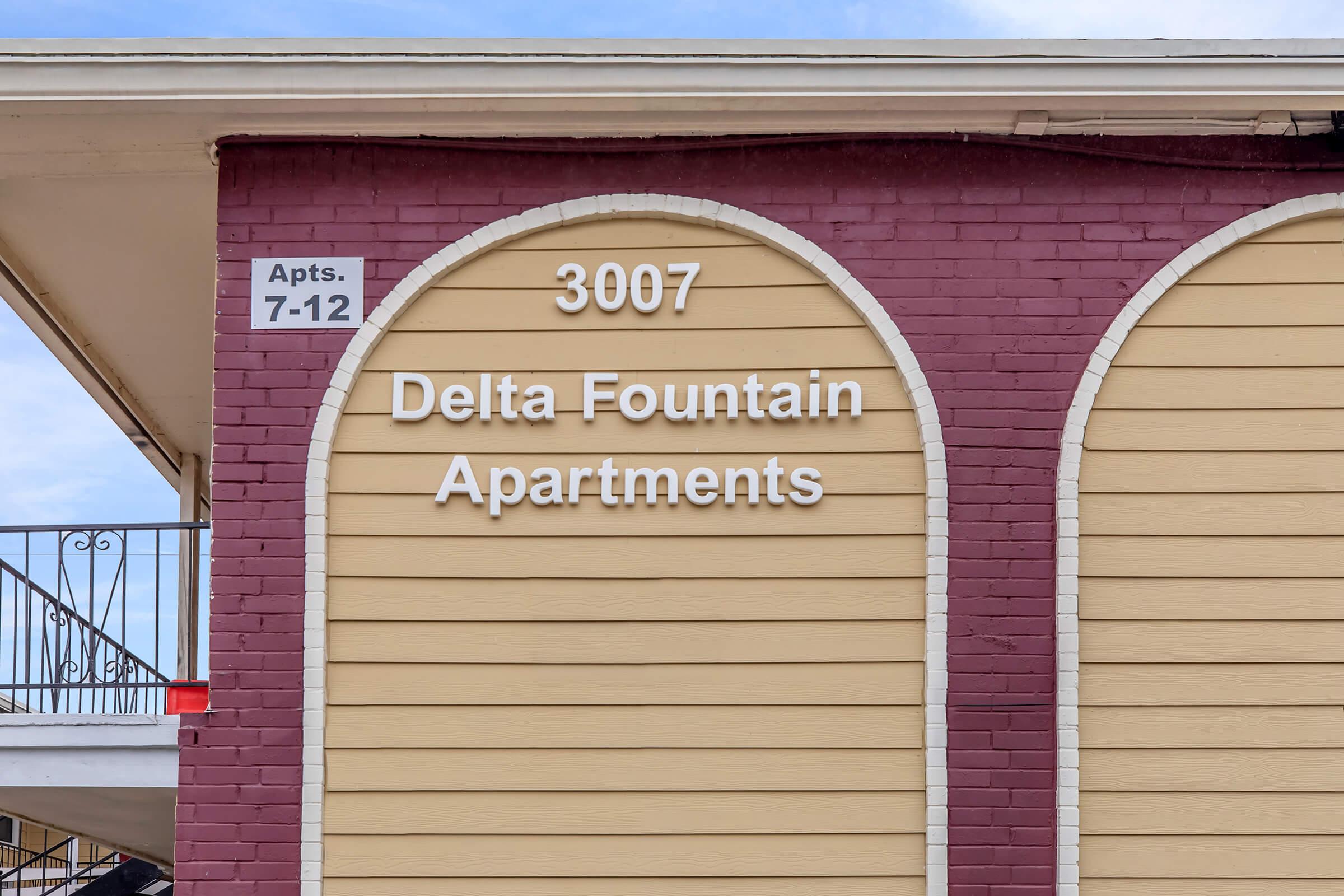 Sign for Delta Fountain Apartments located at 3007, featuring an arched design. The building has a two-tone color scheme with beige and purple hues, and there is a listing for apartments numbered 7-12 visible on the left side.