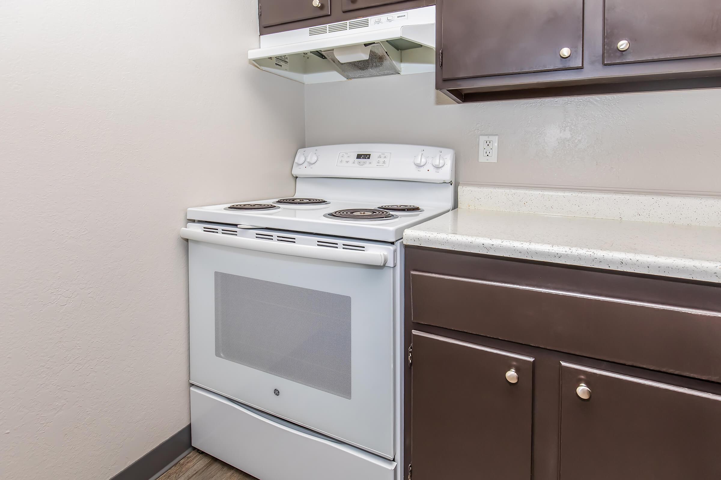A clean, modern kitchen corner featuring a white electric stove with four burners, an overhead microwave, and dark wooden cabinets. The countertop is a light-colored material, complementing the cabinetry while providing a functional cooking space.