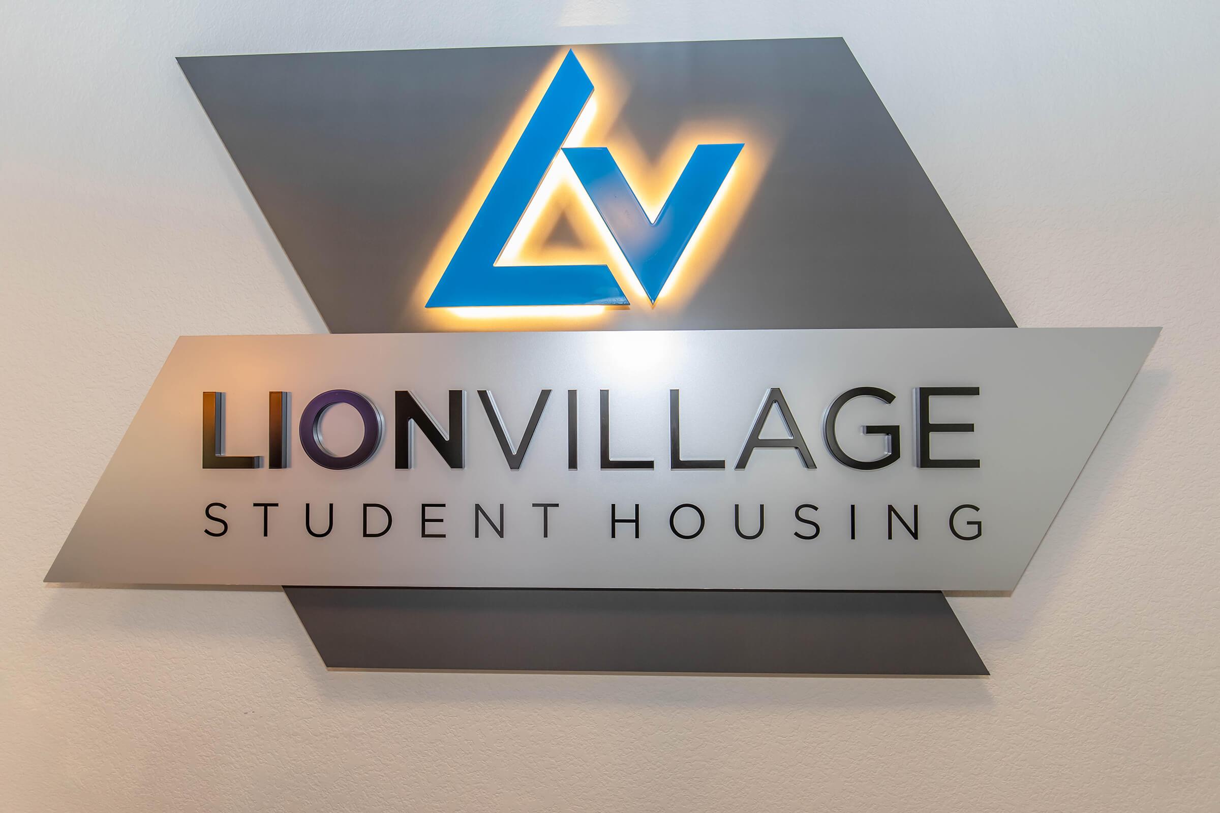 Sign for Lion Village Student Housing, featuring a stylized logo in blue and white. The design includes geometric shapes and a modern font that emphasizes the name and purpose of the facility. The overall appearance is sleek and inviting, suitable for a student accommodation setting.