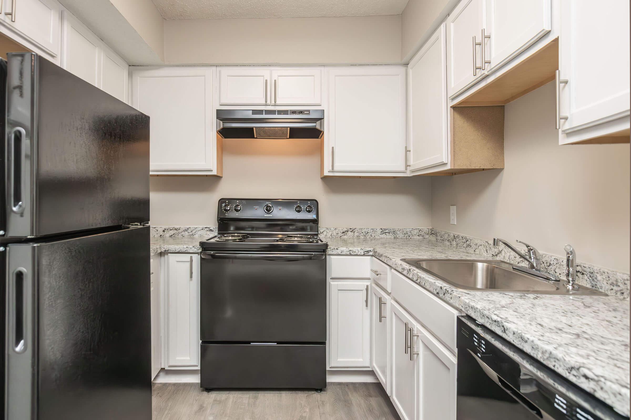 Modern kitchen featuring black appliances including a refrigerator, stove, and dishwasher. White cabinets and light-colored countertops complement the space, which has a neutral wall color. A sink and overhead range hood are included, creating a functional cooking area.
