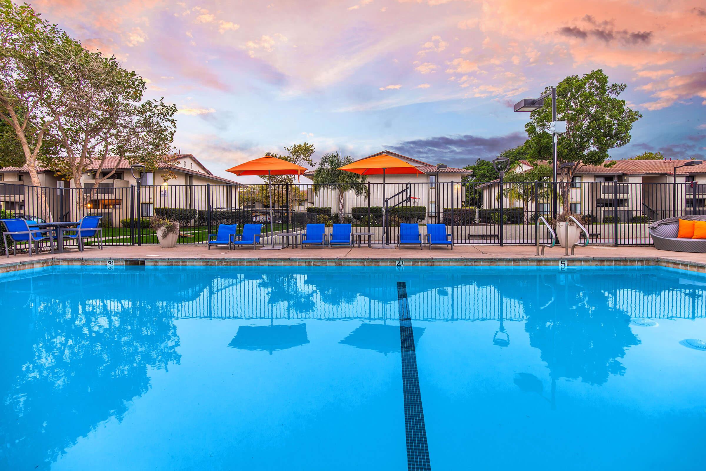 Santa Maria, CA Pet-Friendly Apartments - Cassia - Pool with Orange Umbrellas, Apartment Complex View, and Trees