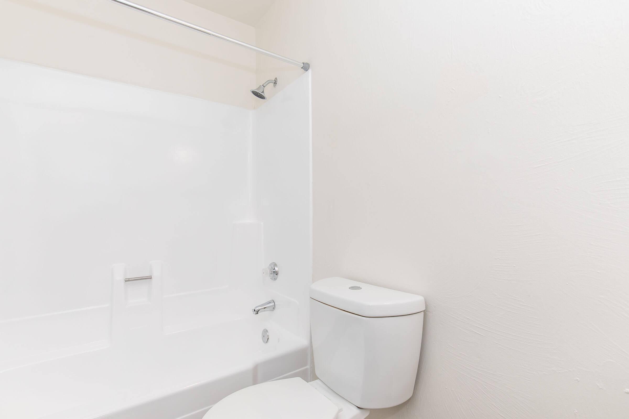 A clean and modern bathroom featuring a white shower with a glass door, a white toilet, and light-colored walls. The space is well-lit and minimalistic, focusing on functionality and simplicity.