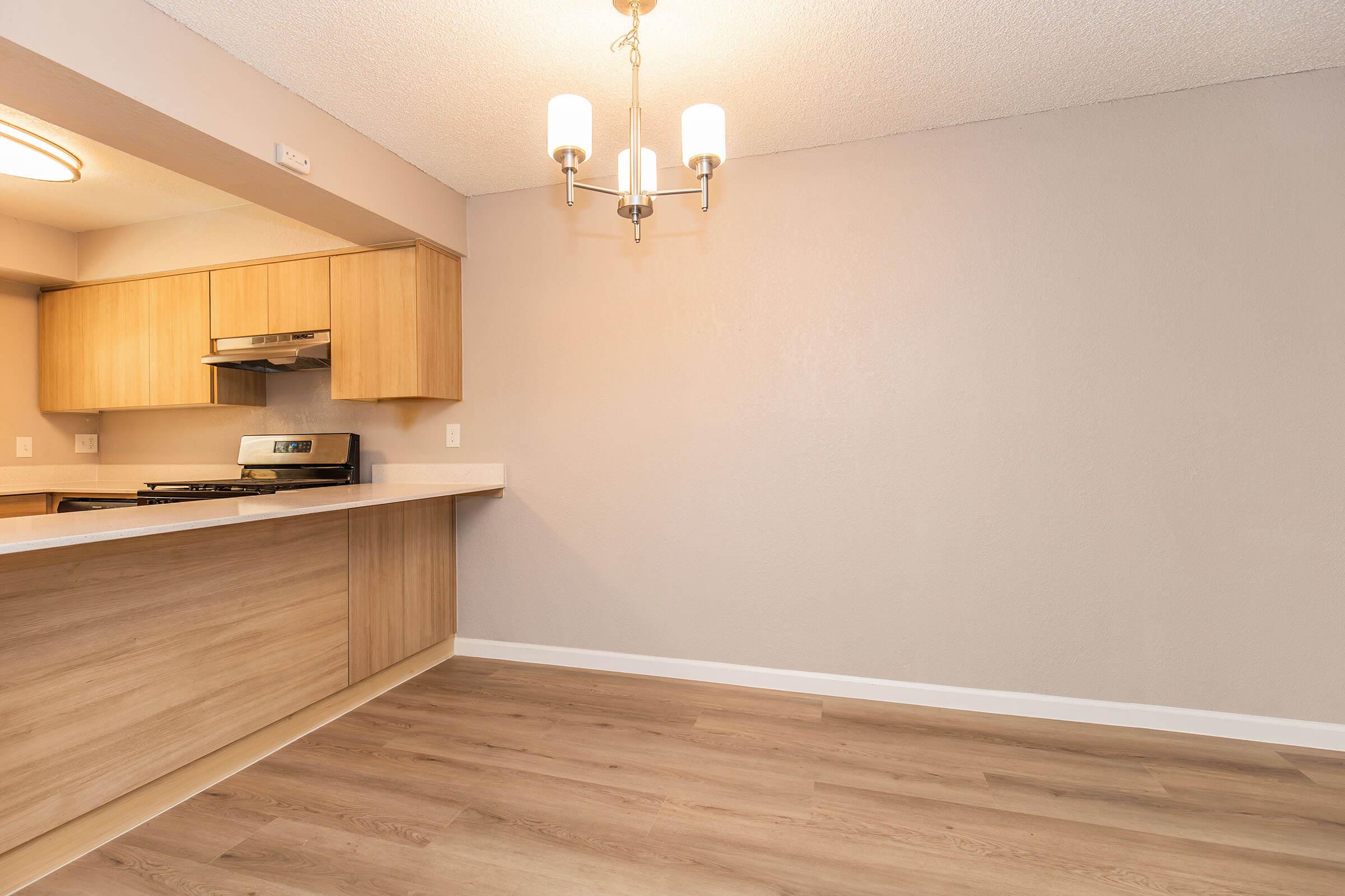 Interior view of a modern kitchen and dining area featuring light wood cabinetry, a countertop, and a pendant light fixture. The walls are painted in a neutral tone, and the floor has a light-colored laminate finish. The space is well-lit, creating an open and inviting atmosphere.