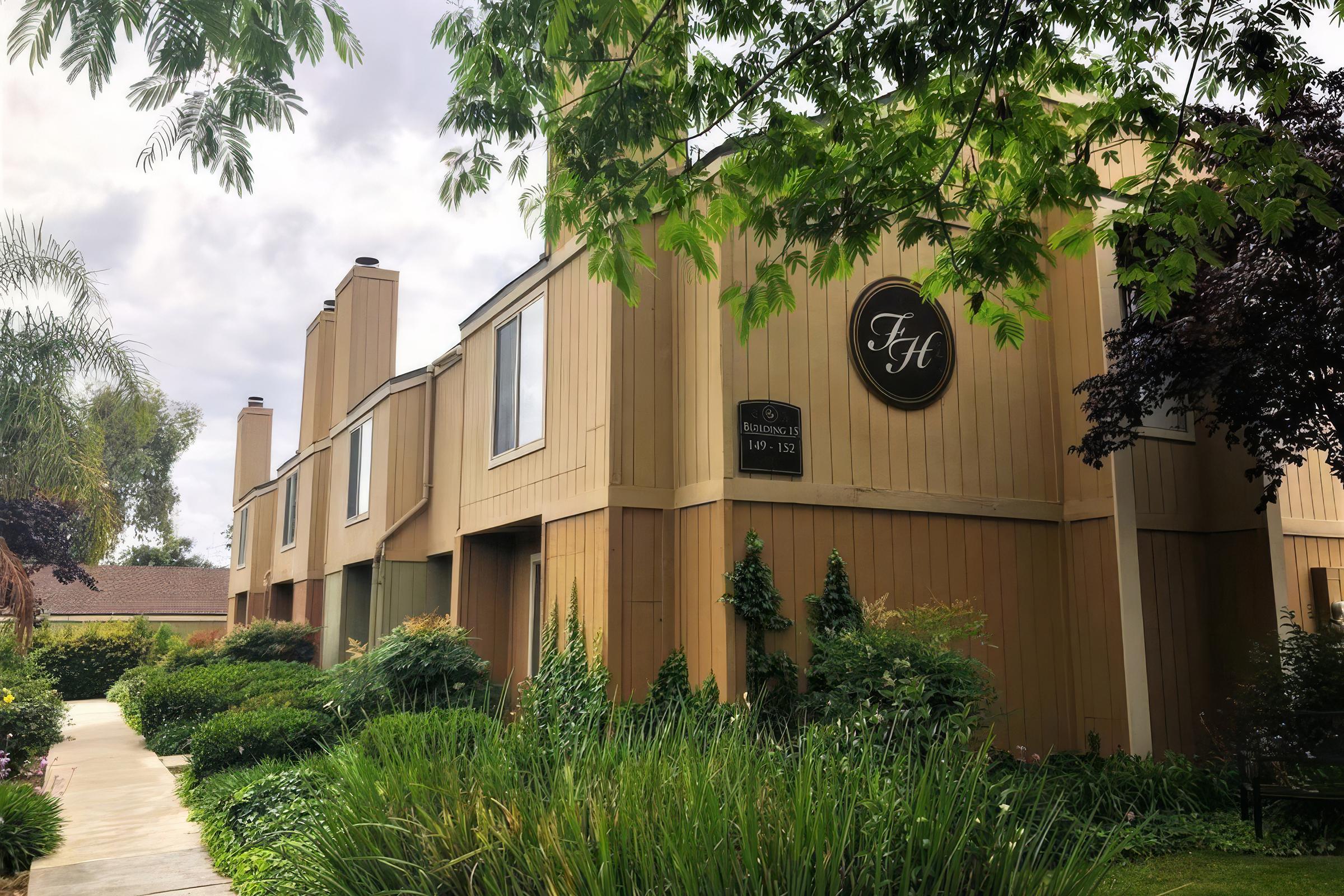 apartment building with pathway to the left and foliage to the right with a cloudy sky