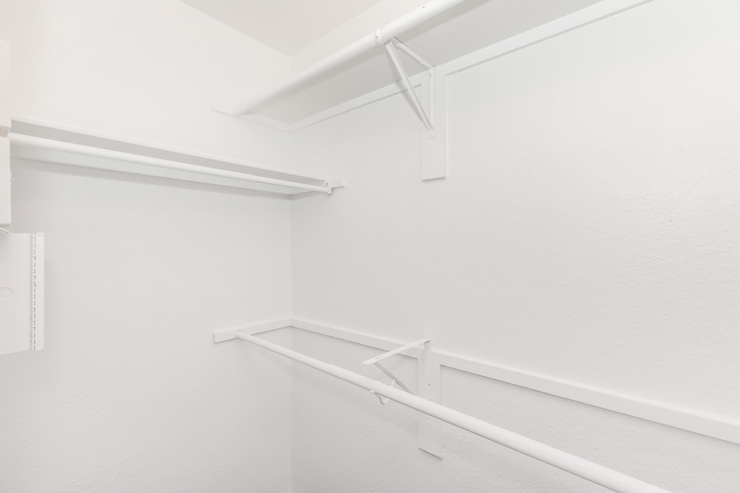 A clean, empty closet featuring white walls and two horizontal hanging rods. The minimalist design provides ample space for organizing clothing and accessories, with no visible items inside.