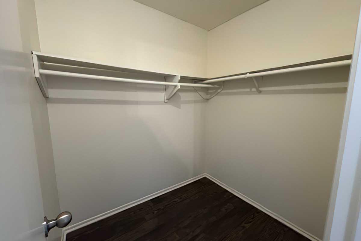 Empty closet with white walls and two shelving units. The floor is dark wood, and there is a door partially visible on the left. The space is well-lit and offers a clean, minimalistic appearance.