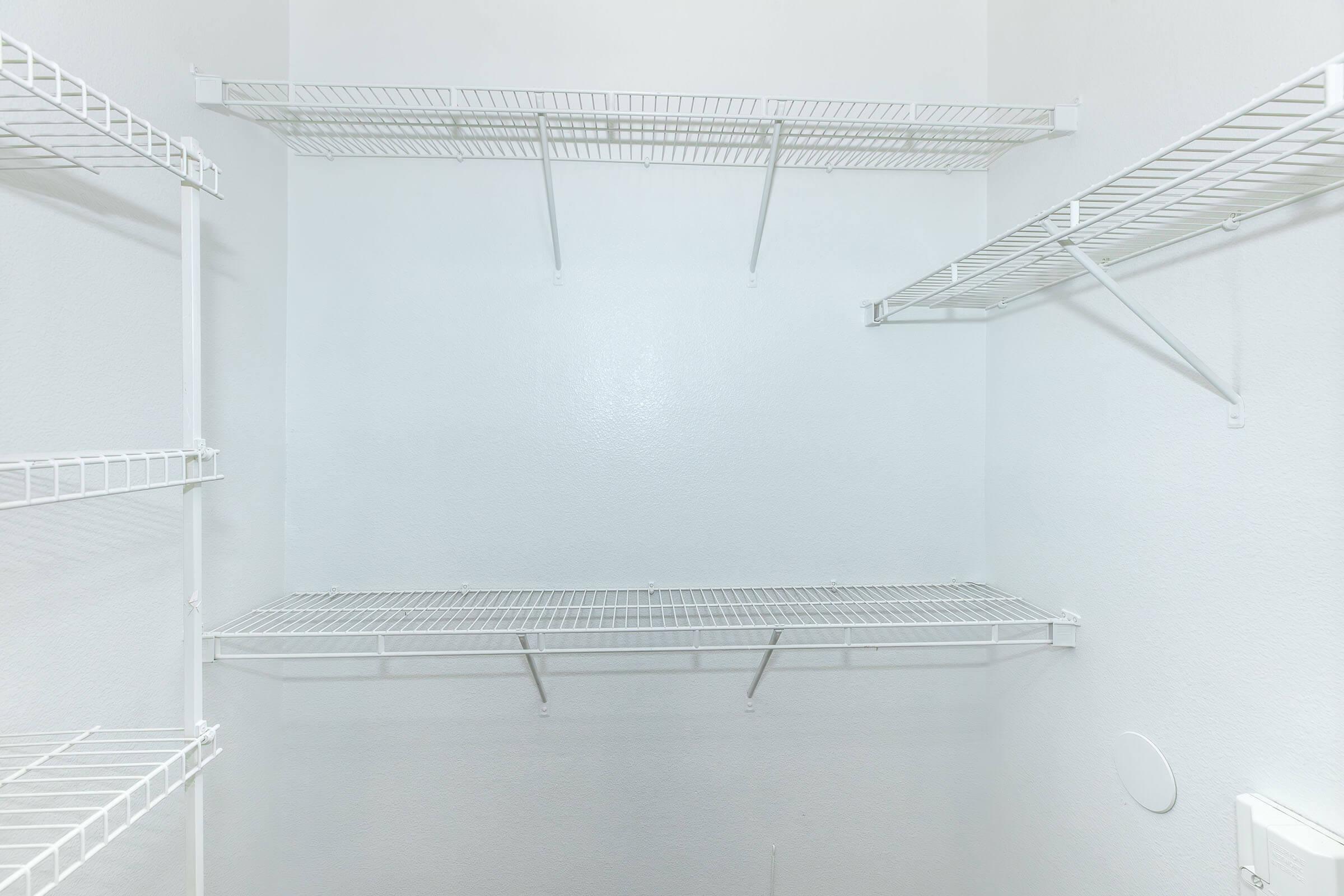Empty closet with white walls and several wire shelving units mounted on the walls, providing storage space. There are no items or additional decorations present in the closet, creating a clean and minimalist appearance.