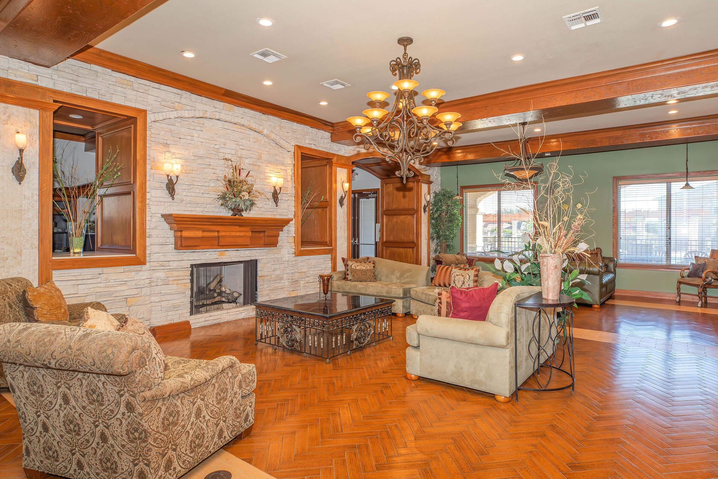 A luxurious living room featuring elegant seating arrangements with patterned and solid-color sofas, a decorative coffee table, and a stone fireplace. The room has warm wooden accents, large windows allowing natural light, and tasteful decor elements like plants and chandeliers, creating a cozy and inviting atmosphere.