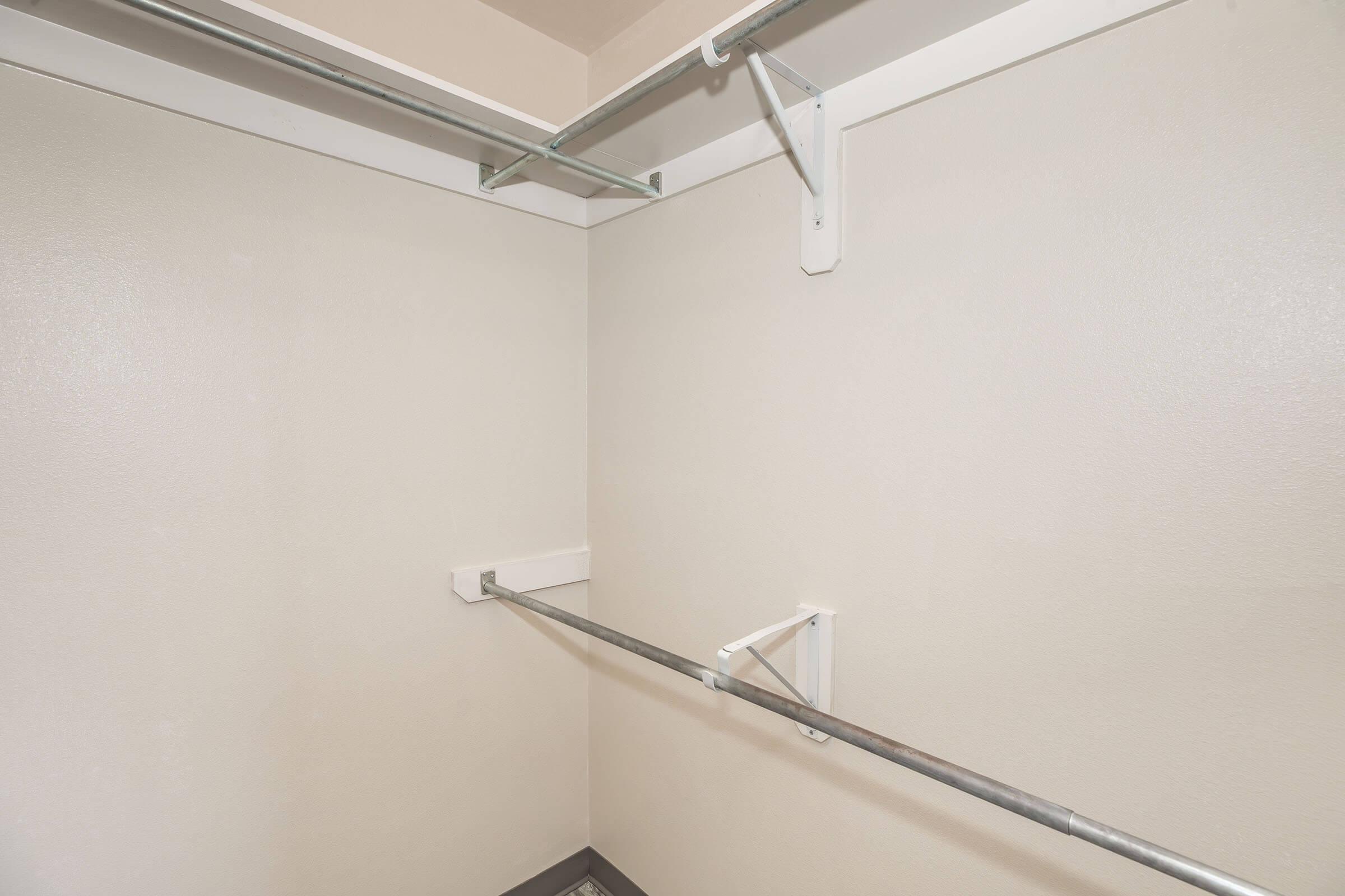 An empty closet featuring beige walls, a single hanging rod, and wall-mounted shelving. The space is clean and uncluttered, with neutral colors creating a simple and open appearance. The floor is not visible in the image.