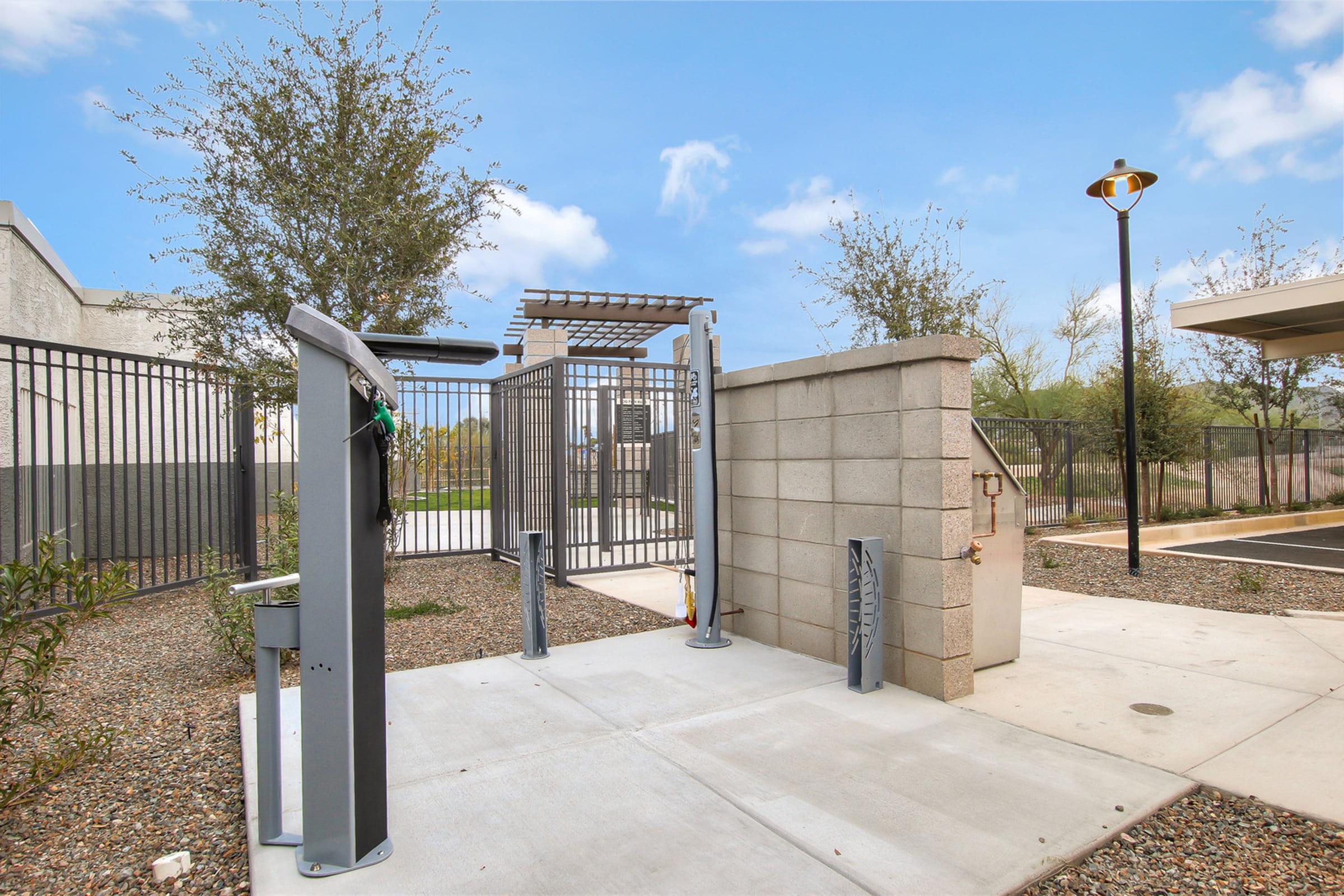 A modern outdoor entrance gate with metal fencing, surrounded by gravel landscaping and small plants. There’s a pathway leading to the gate, with a lamppost on the right. 