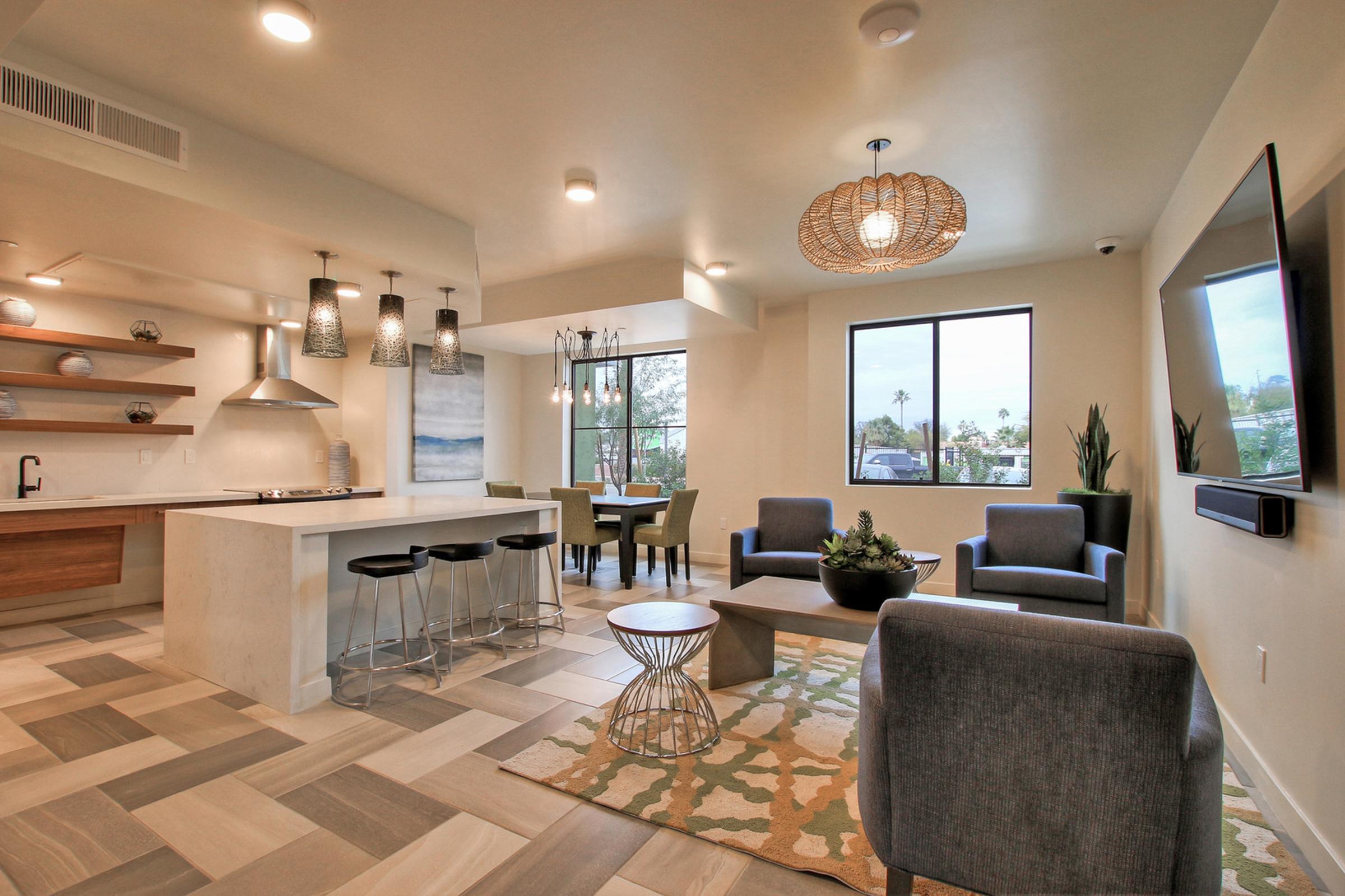 Modern living room with a neutral color palette, featuring a kitchen island, bar stools, and a dining area.
