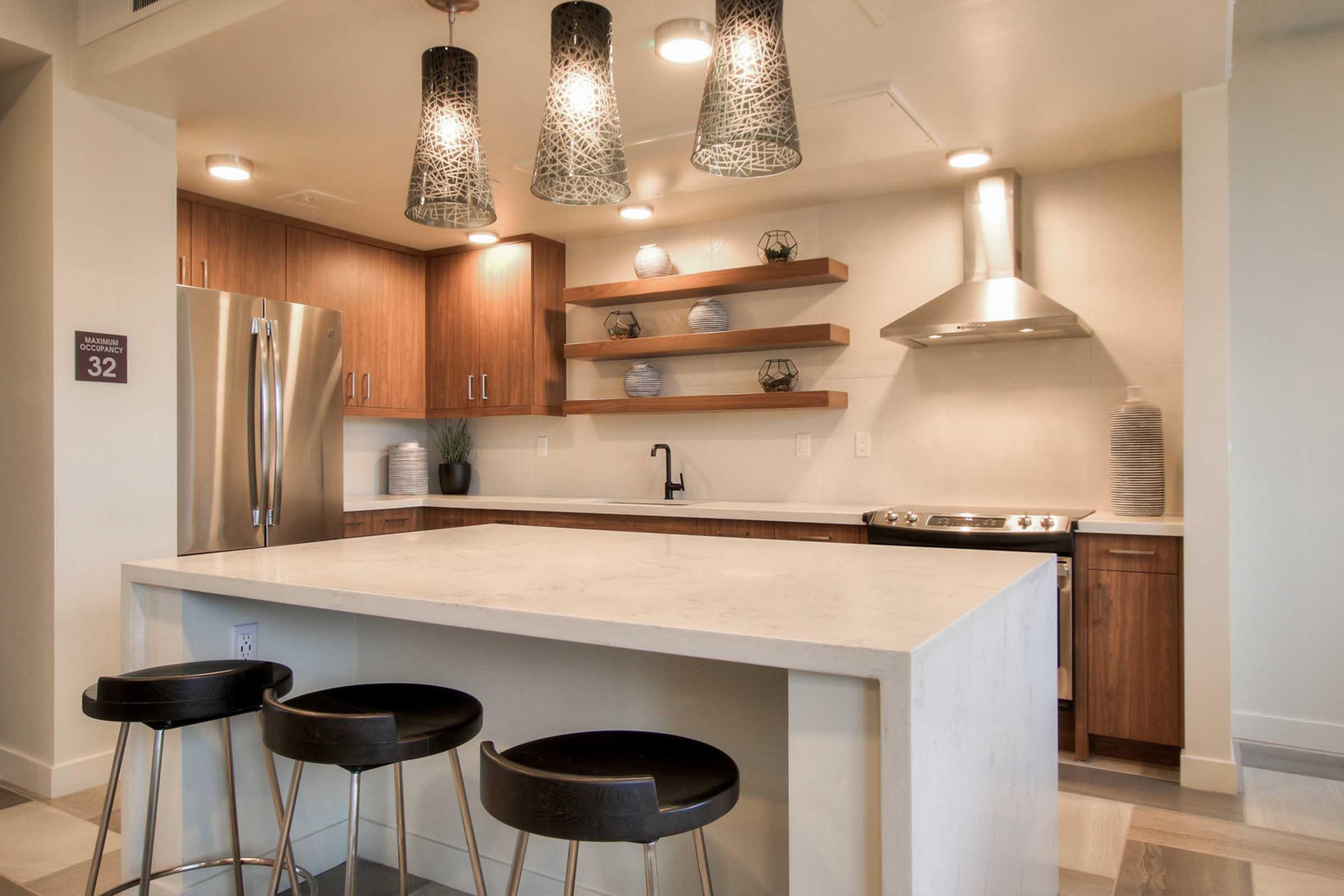 Modern kitchen featuring a large island with a white countertop and black barstools. The space has wooden cabinetry with open shelves displaying decorative vases. 