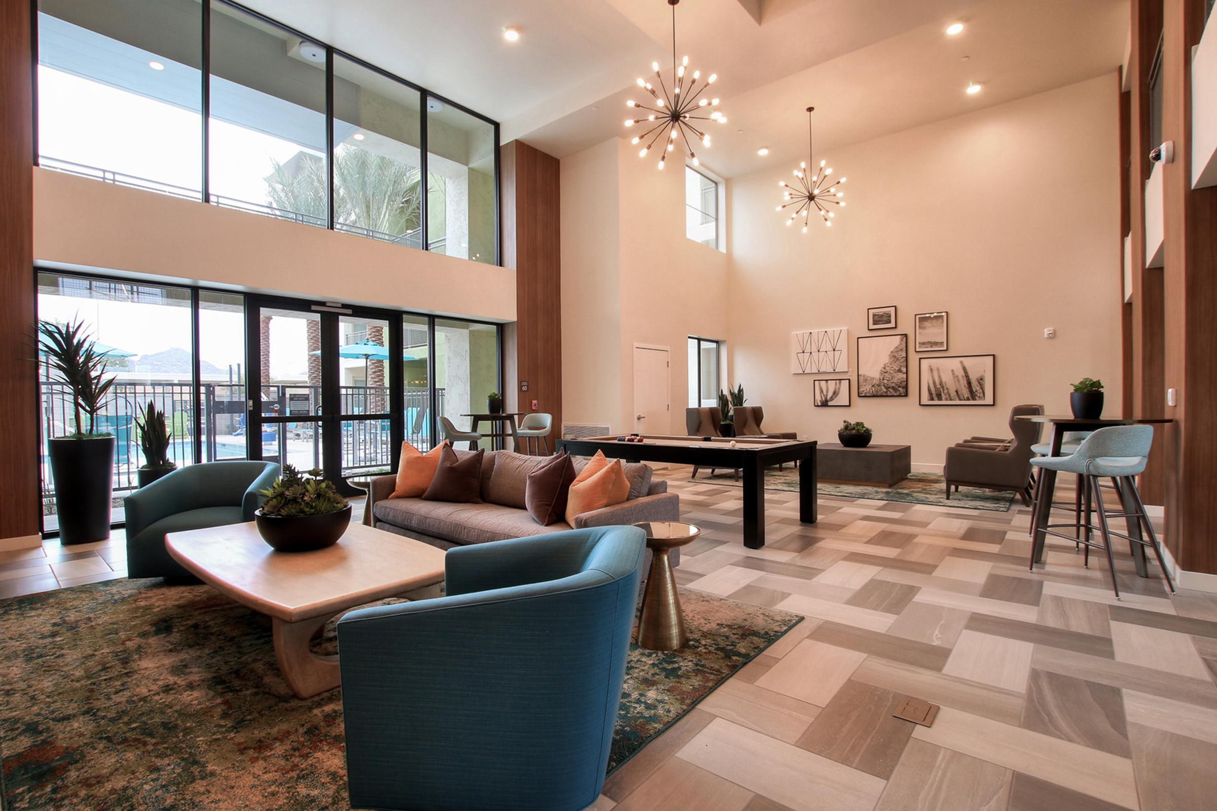 A modern, spacious lobby area featuring large windows that let in natural light, contemporary furniture including a sofa, armchairs, and a coffee table.