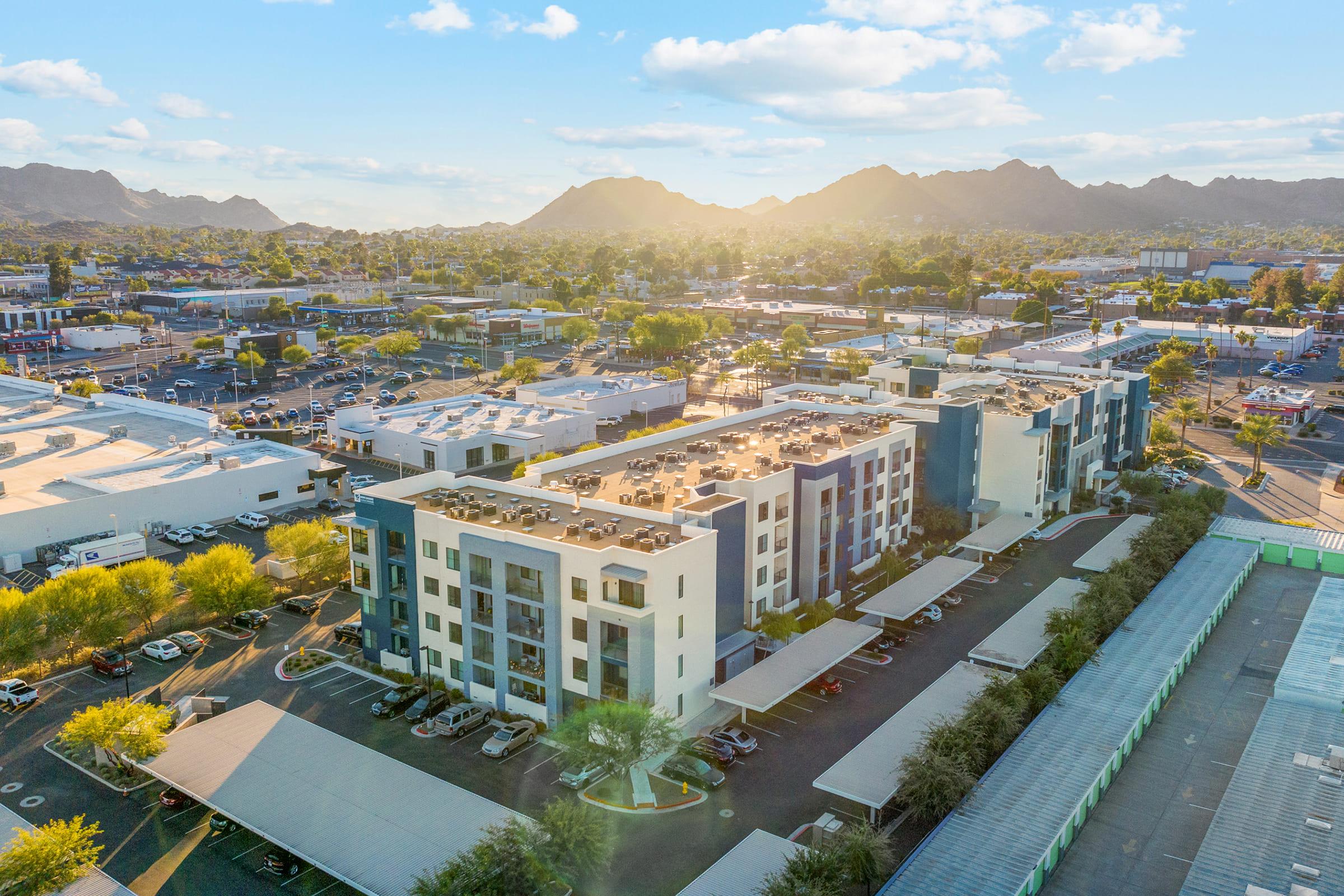 Aerial view of a modern multi-story residential building surrounded by commercial buildings and parking lots. 