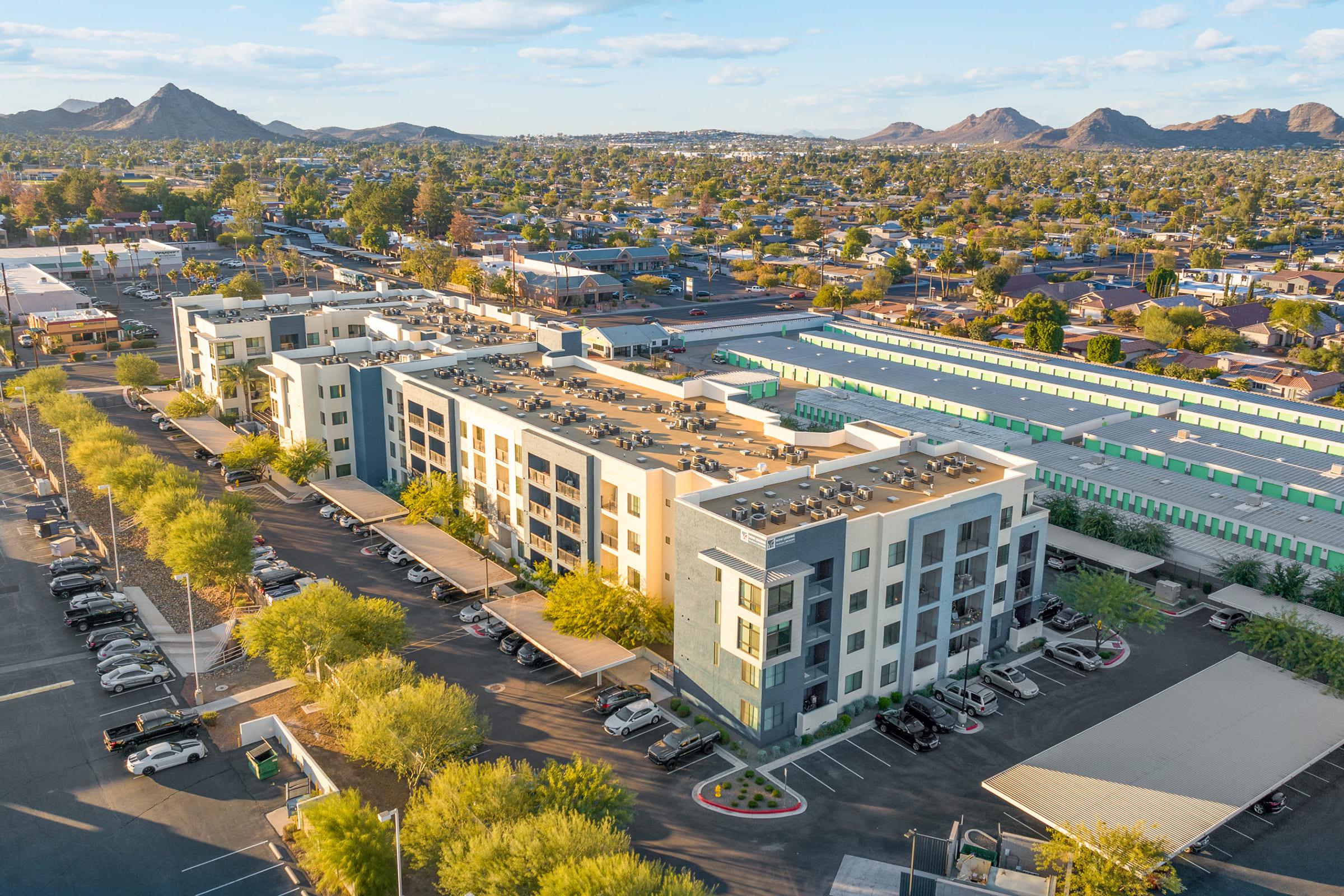 Aerial view of a modern apartment complex with multiple stories, surrounded by trees and a parking lot.