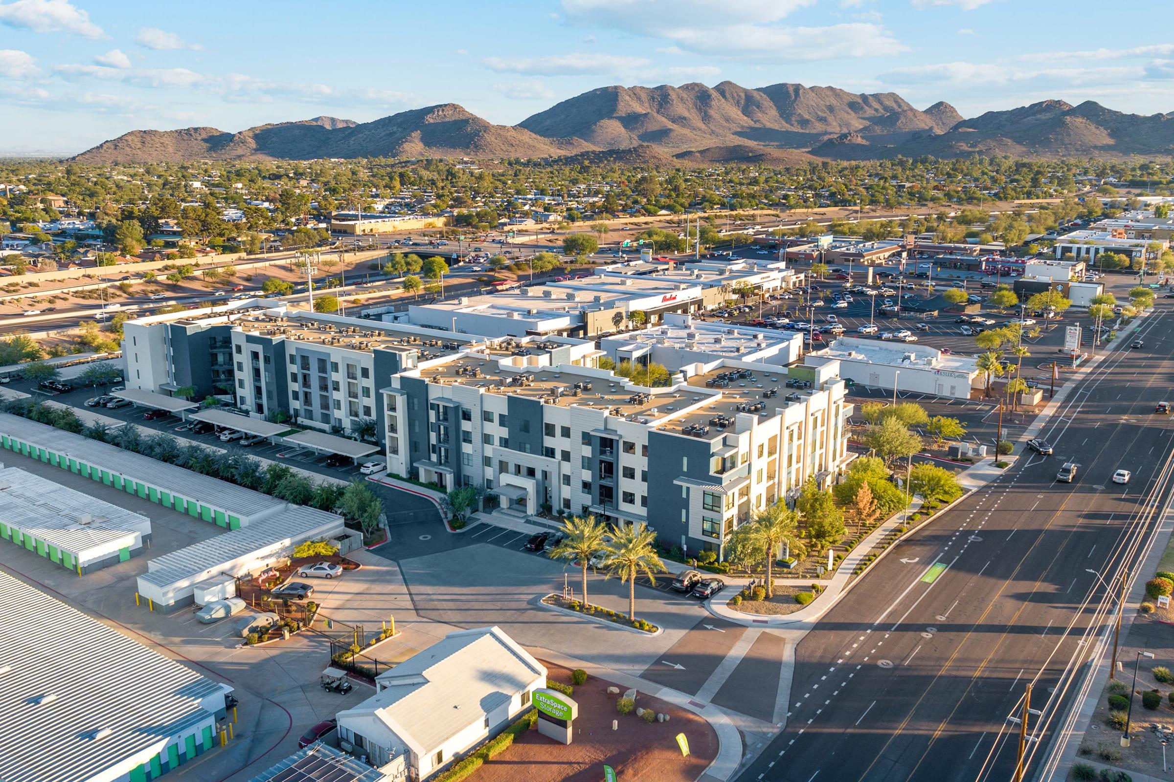  Aerial view of a modern multi-story building with a landscaped area, set against a backdrop of mountains and clear blue skies. 