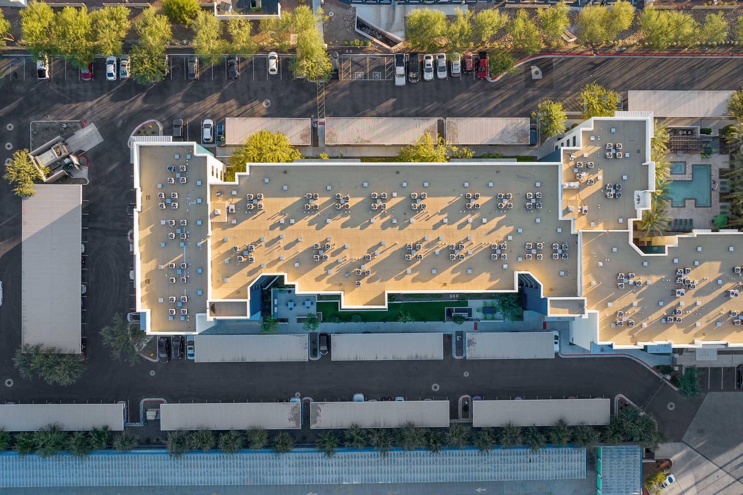 Aerial view of a large building with a flat roof, featuring numerous chairs and tables arranged in outdoor seating areas. 