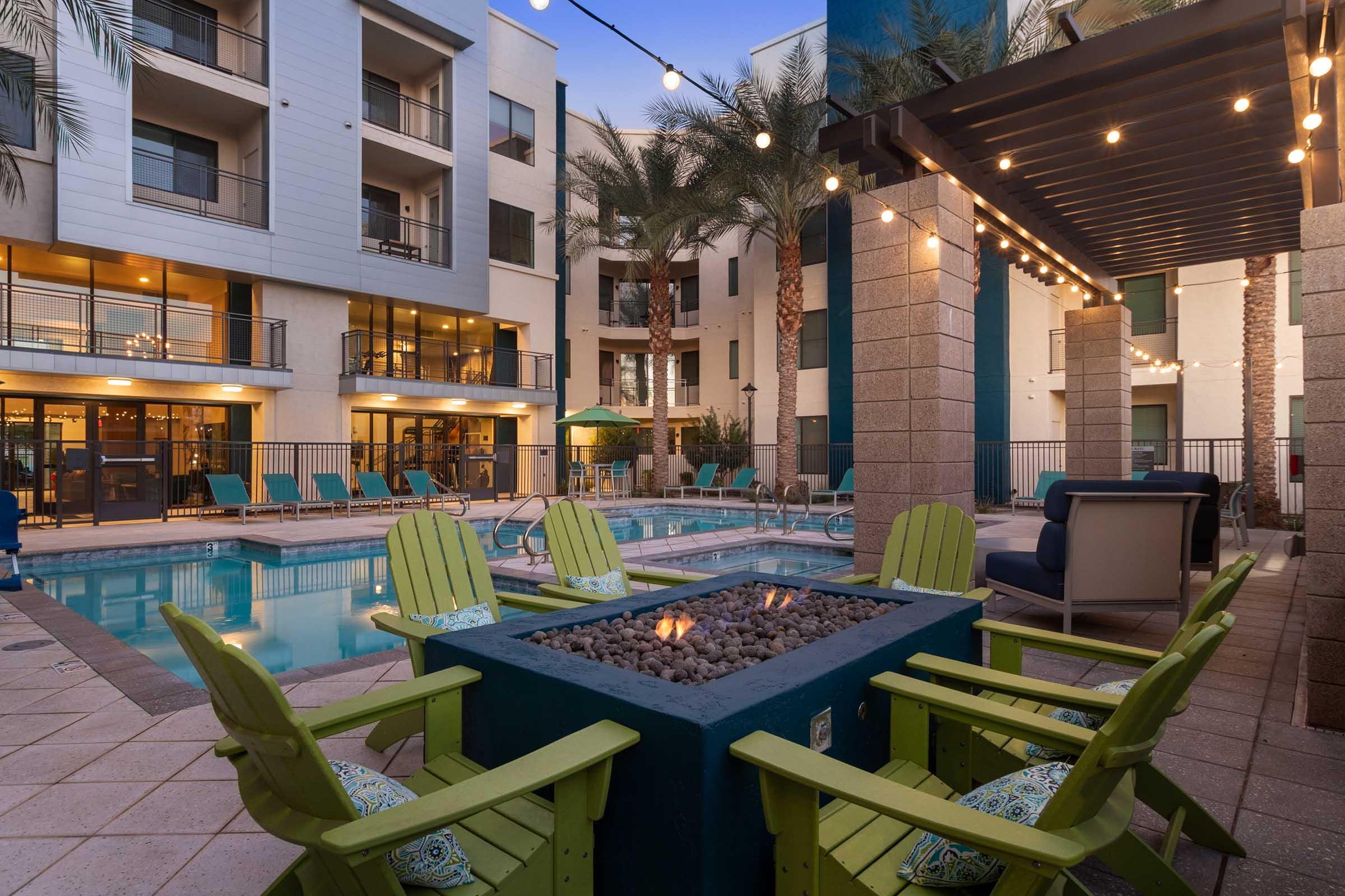 View of a landscaped pool area featuring a fire pit surrounded by bright green chairs.