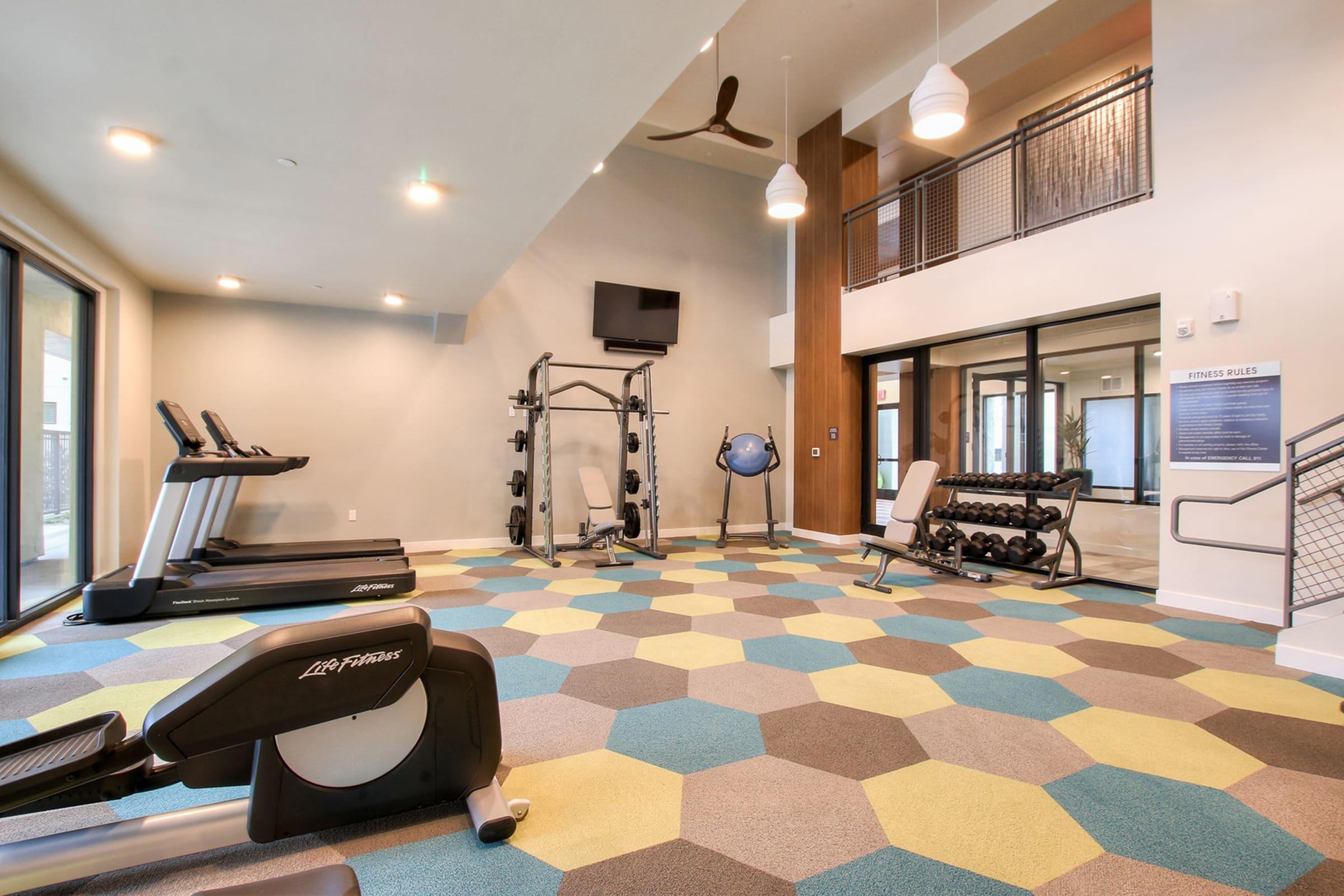 A modern gym with exercise equipment including treadmills, a cable machine, and a weight bench. 