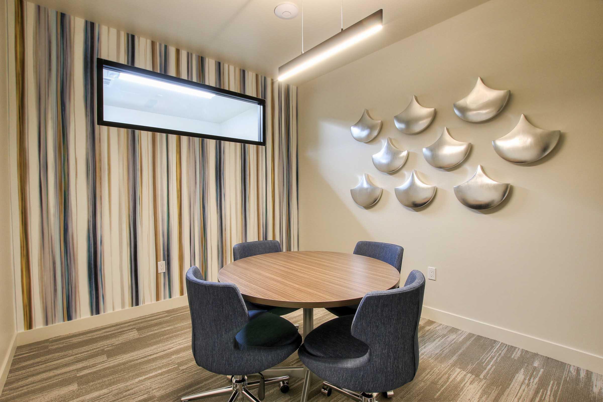 Interior view of a small meeting room featuring a round wooden table with four chairs. 