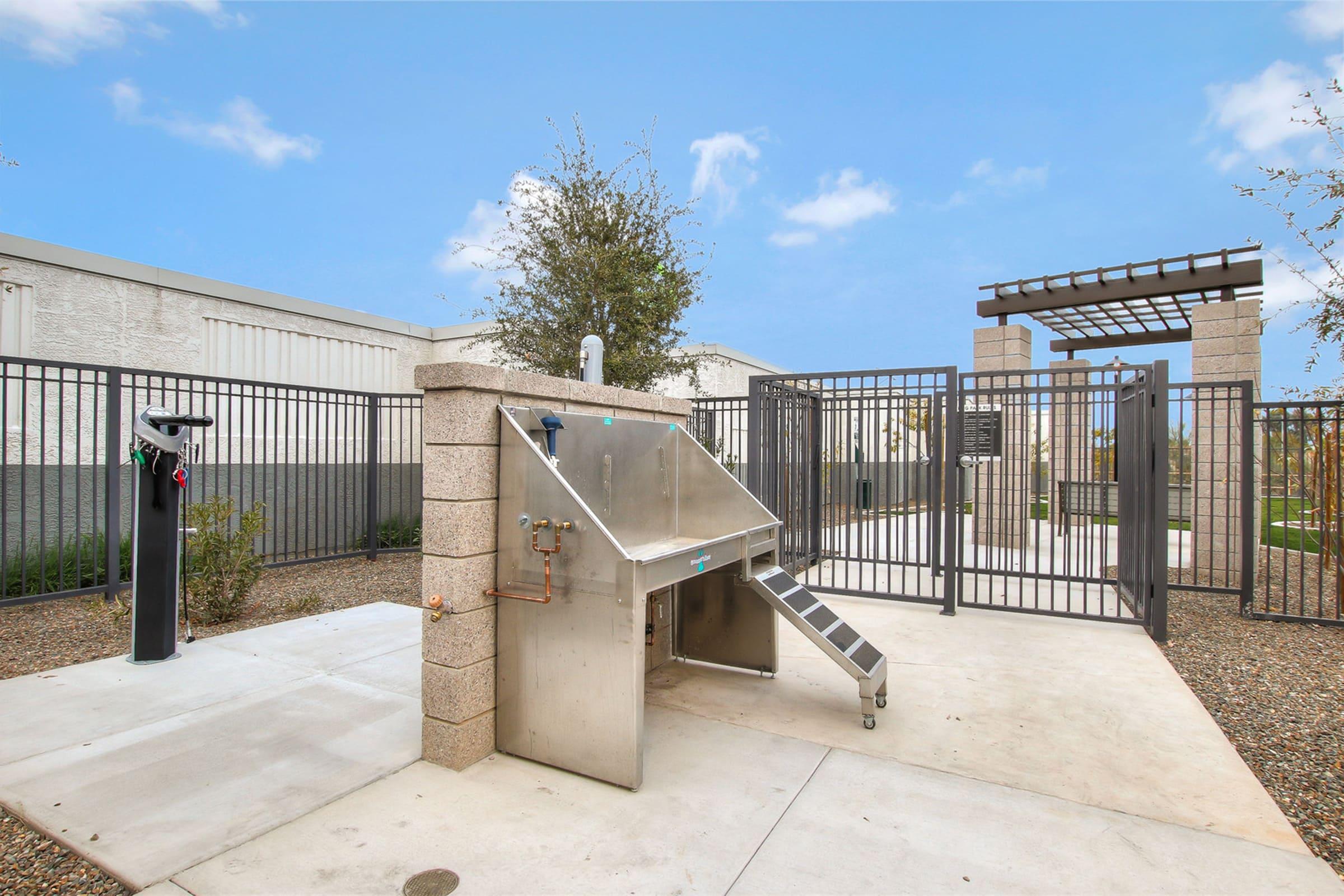 A stainless steel dog washing station with a ramp, located in a fenced outdoor area. 
