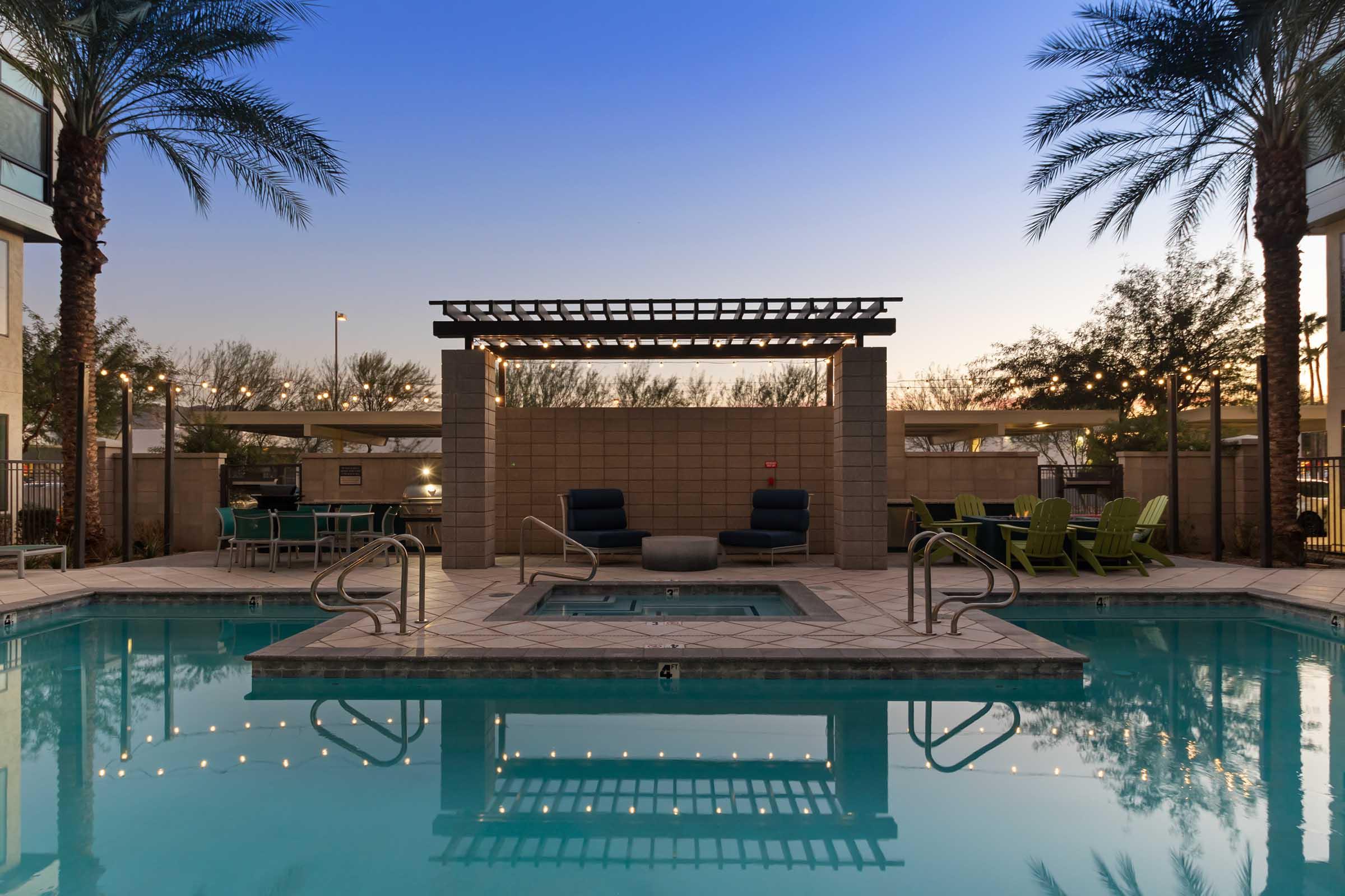 A serene pool area at dusk, featuring crystal-clear water, a hot tub, and comfortable lounge chairs. 