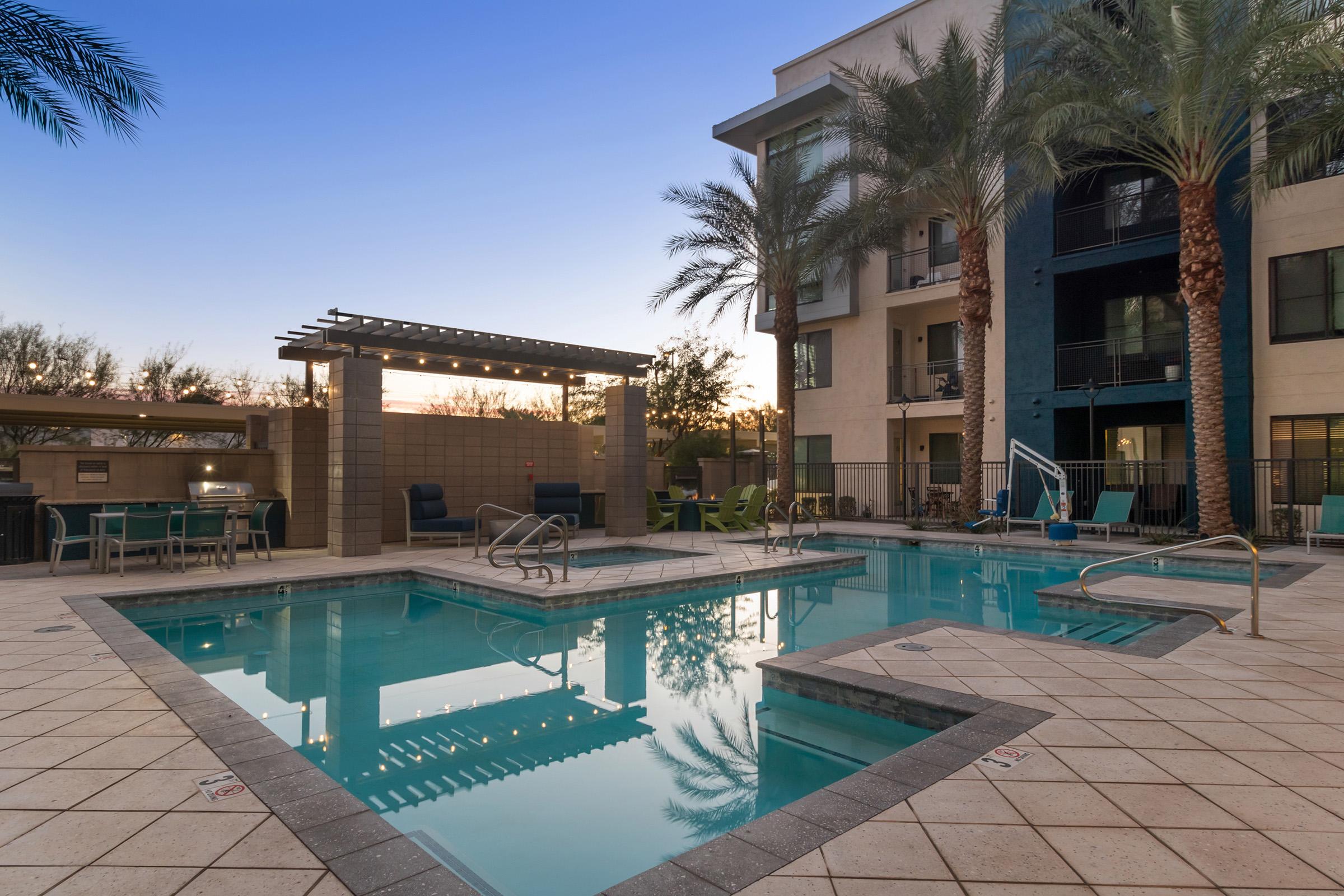 A serene swimming pool area featuring two connected pools, surrounded by palm trees and modern architecture. 