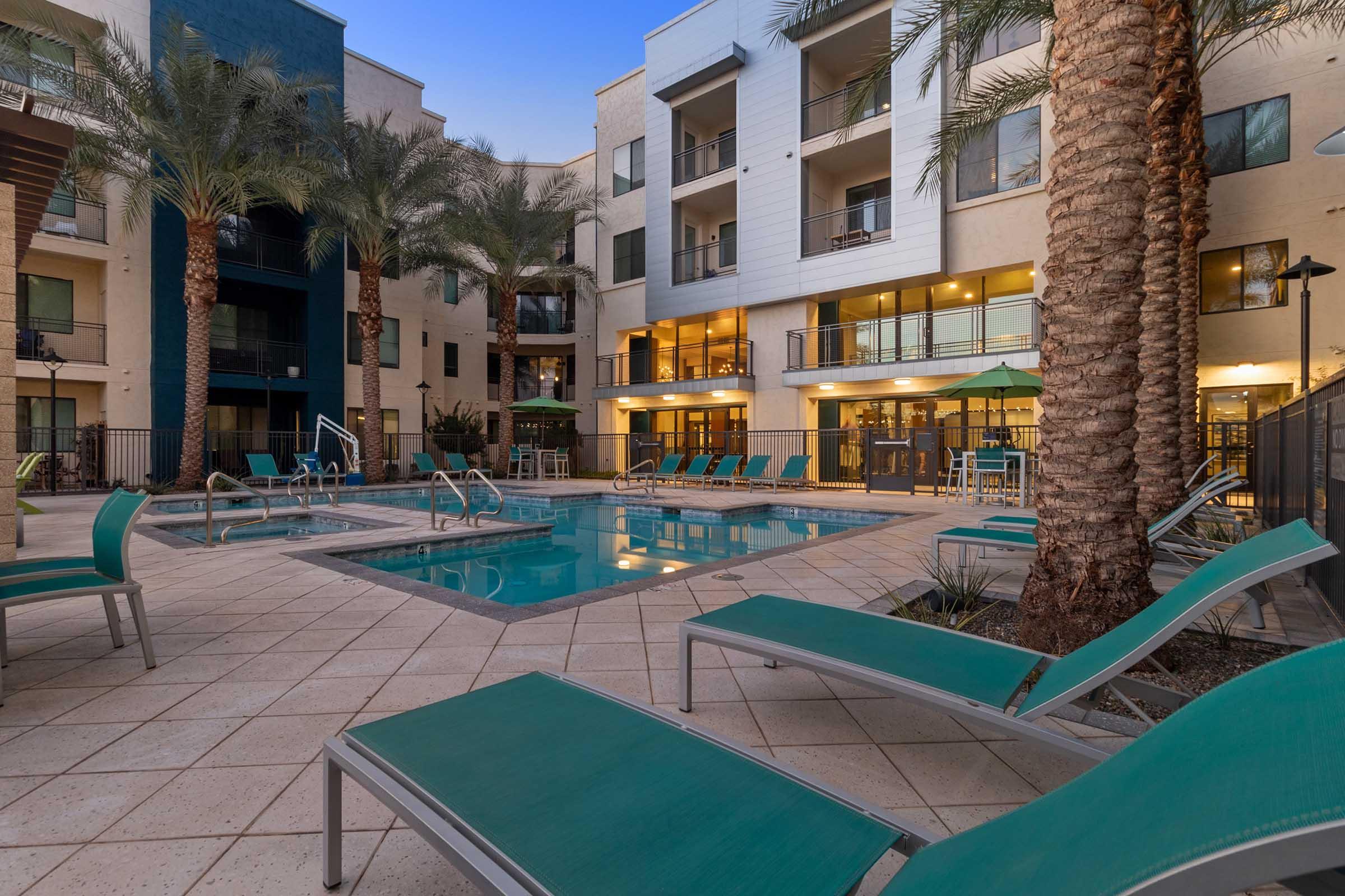 A modern pool area surrounded by palm trees and lounge chairs, featuring a rectangular swimming pool and a hot tub. 