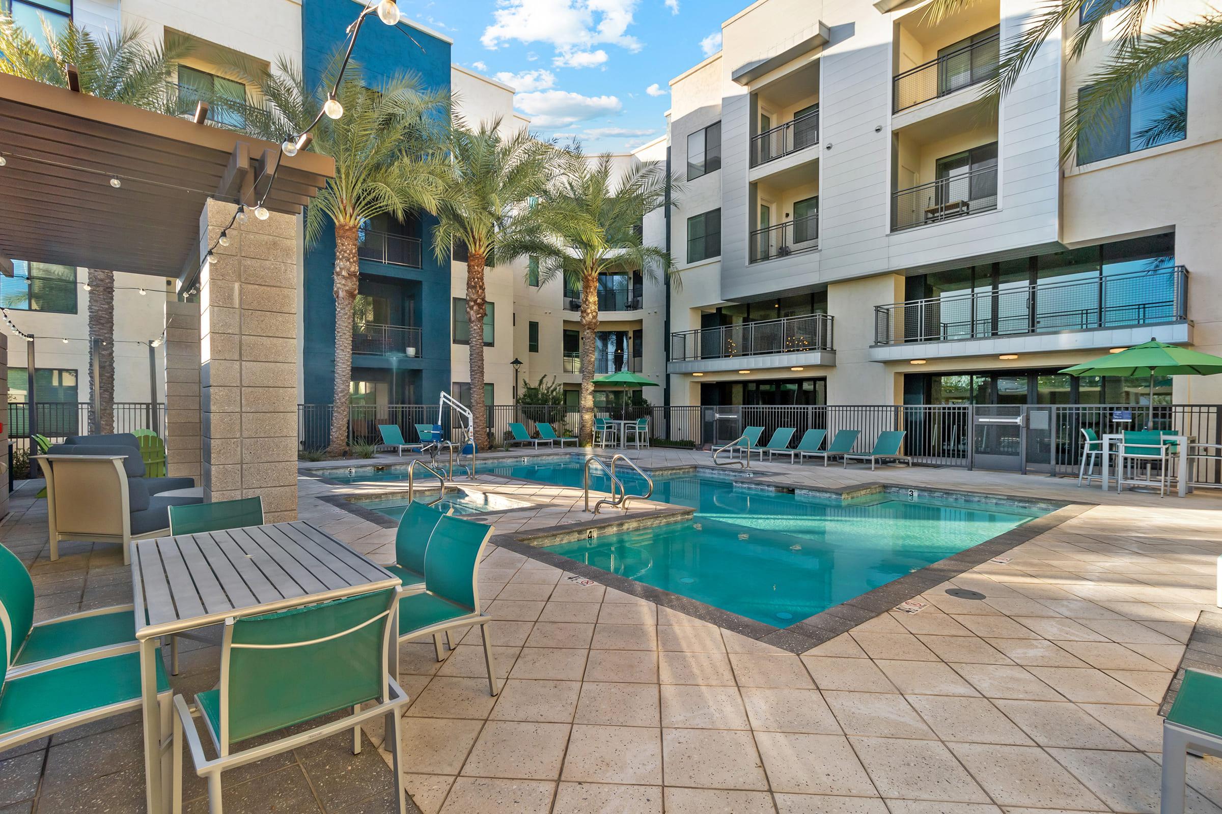 A sunny courtyard featuring a swimming pool surrounded by lounge chairs and tables. 