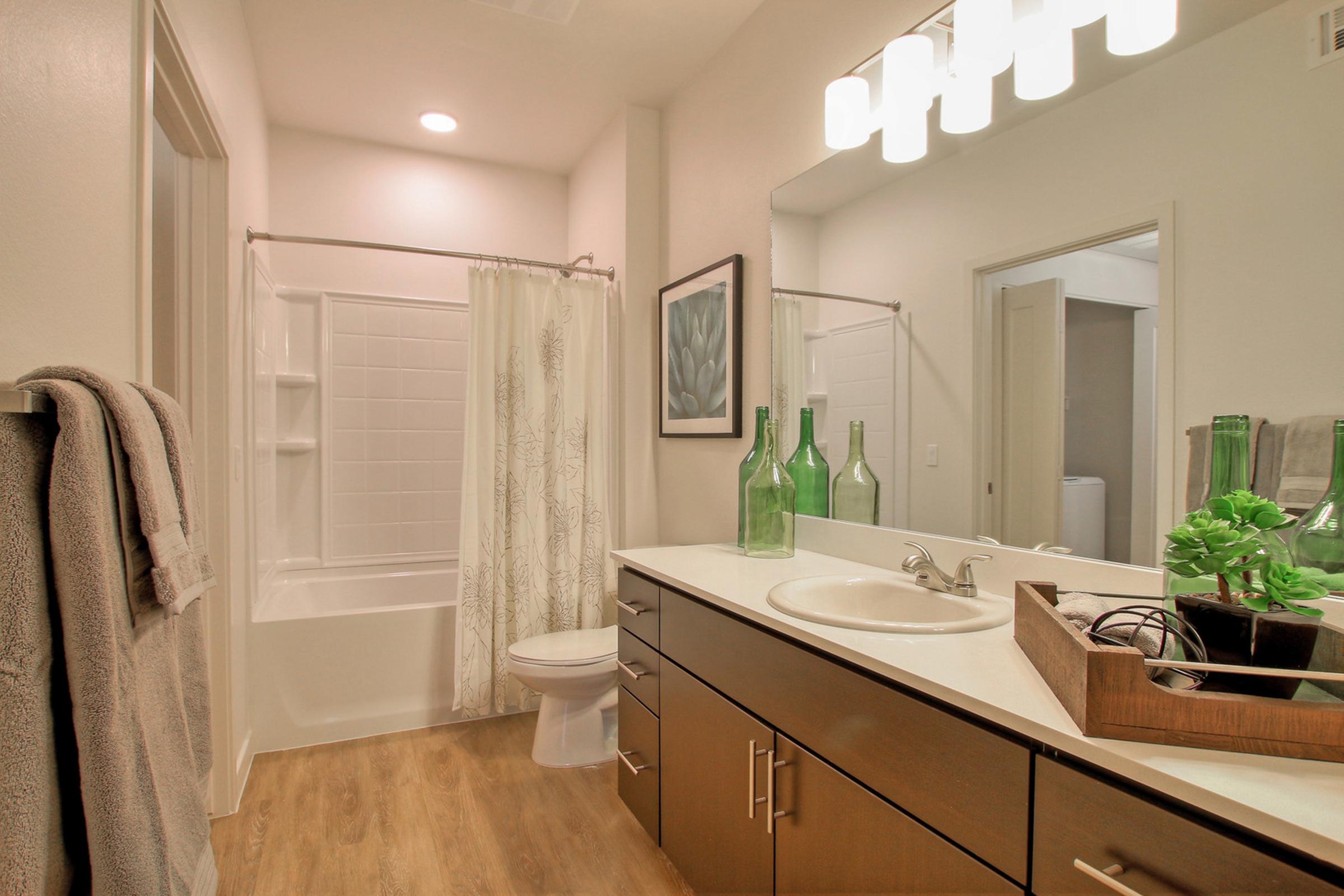 A modern bathroom featuring a white bathtub with a shower curtain, a sleek vanity with a sink, and wooden cabinetry. 
